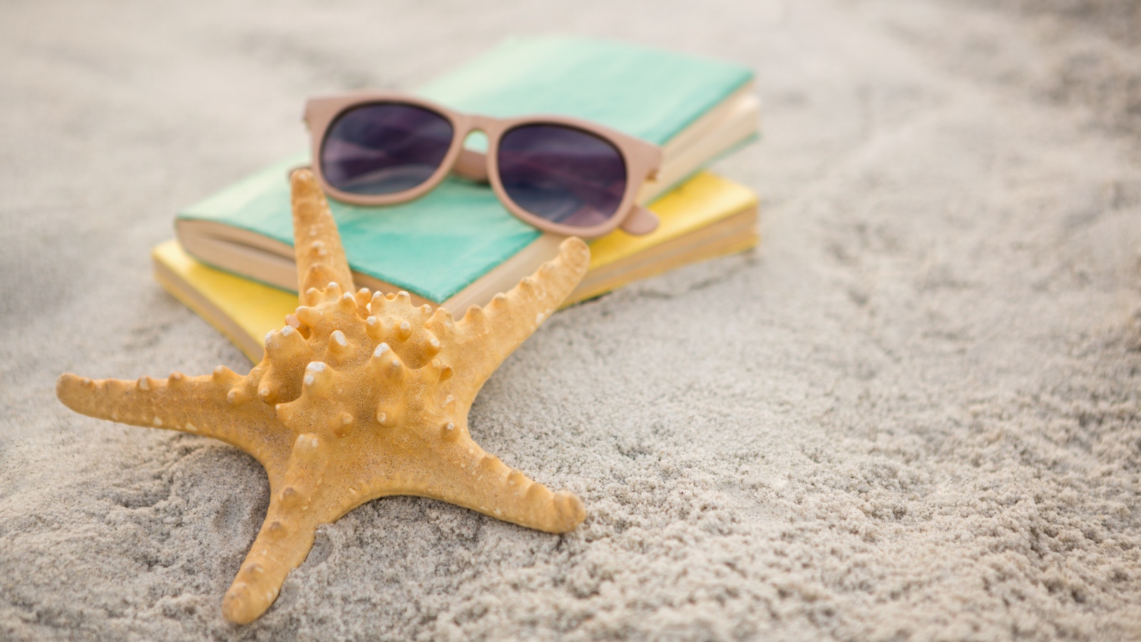 Книги, очки и морская звезда на белом песке 