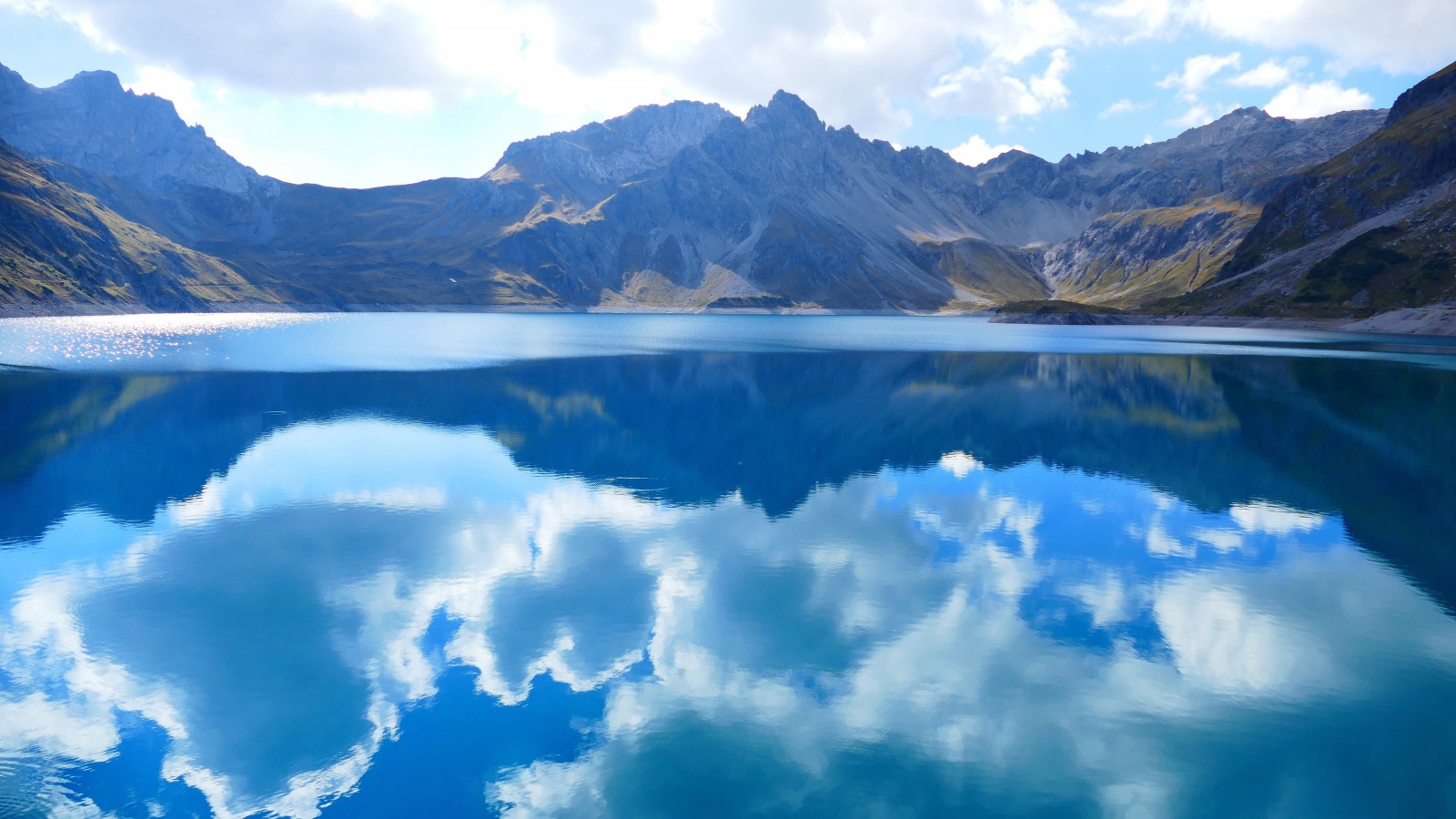 Beautiful white clouds are reflected in the water of the lake against the background of mountains