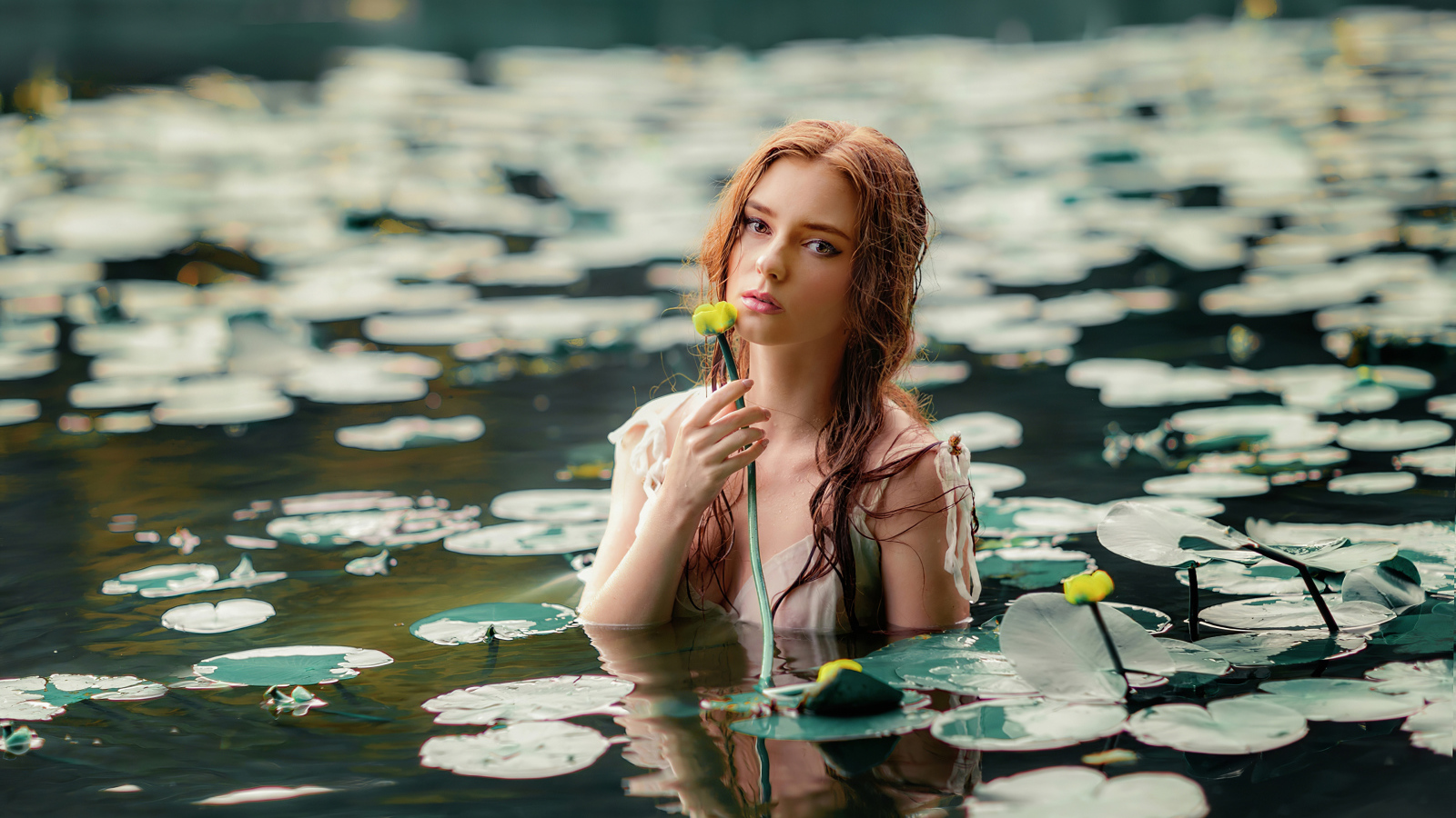 Красивая молодая девушка с водяными лилиями в пруду