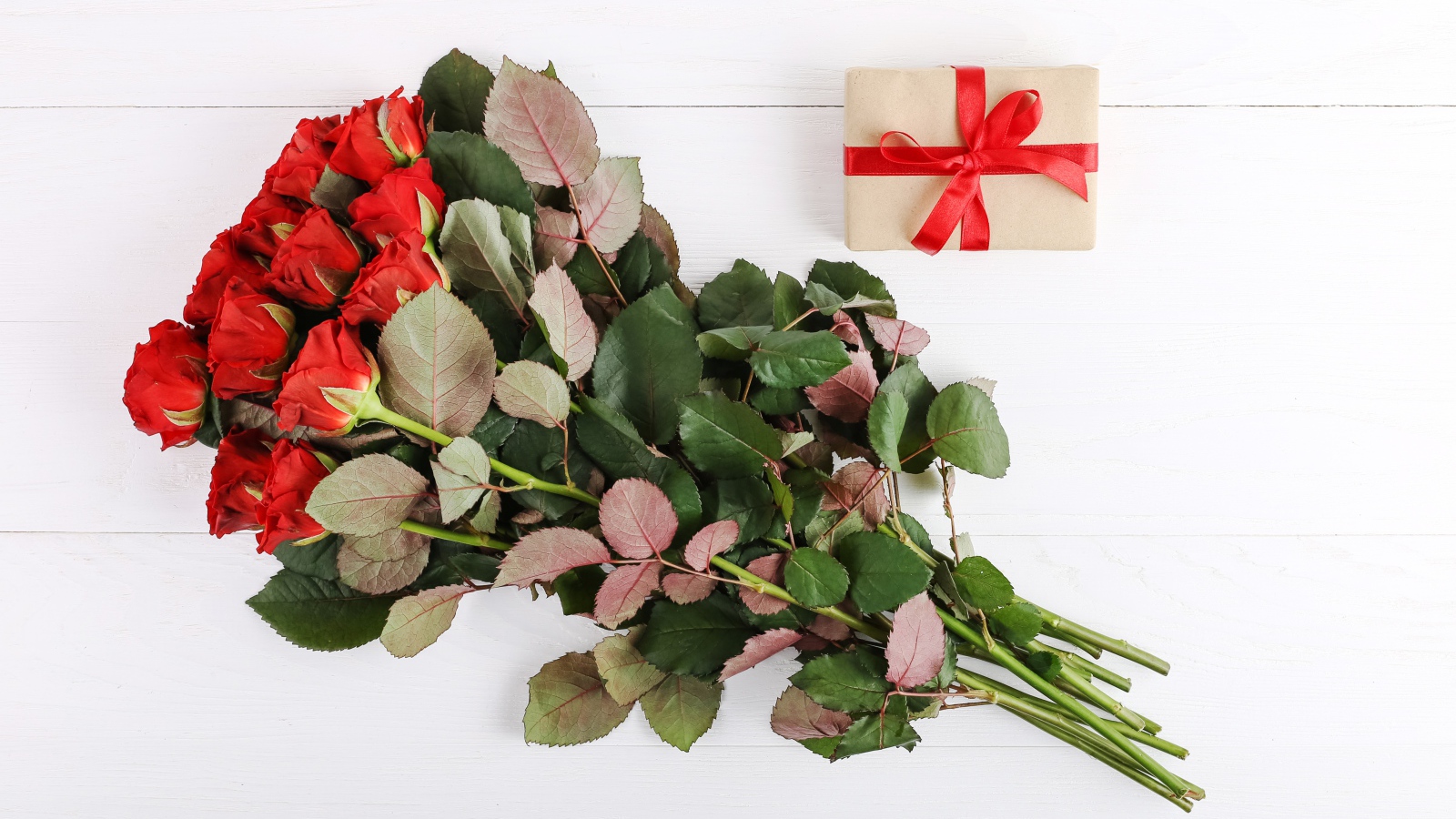 Букет колючих красных роз с подарком на белом фоне