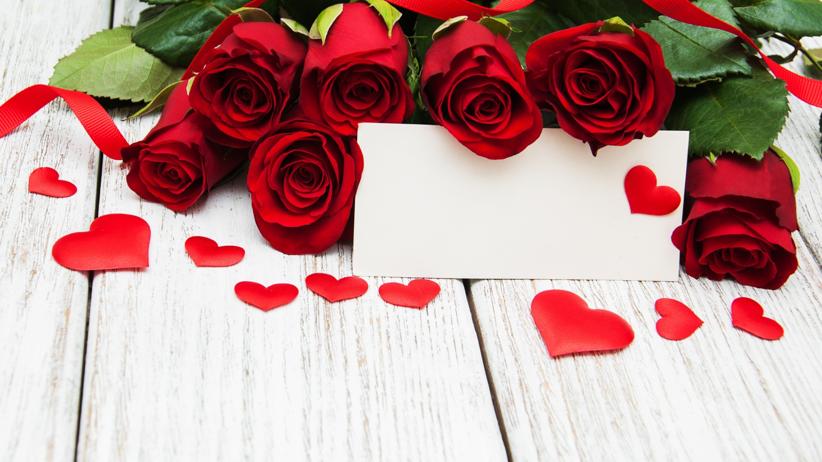 Букет красных роз на столе с сердечками и открыткой