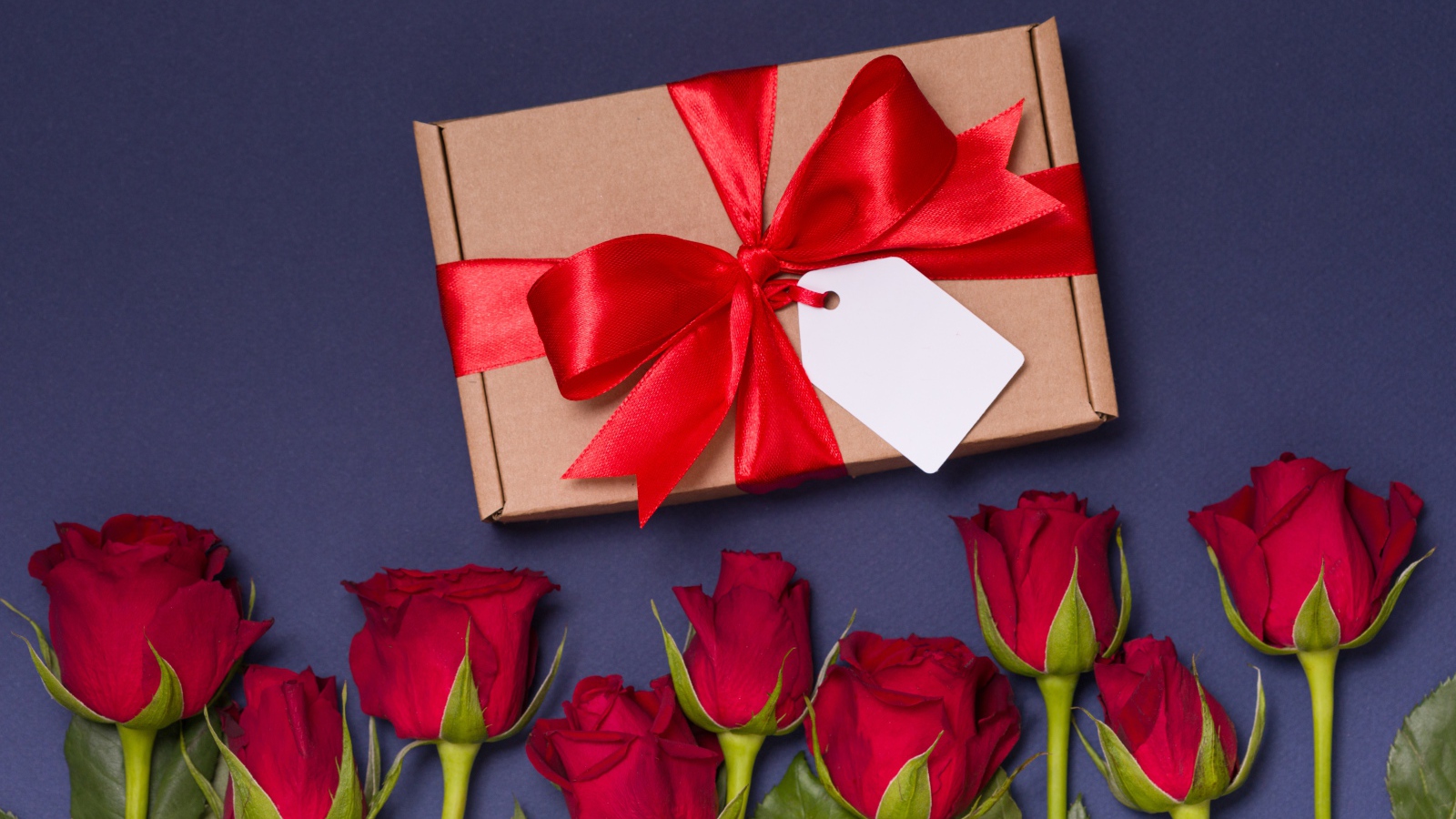 Подарок с красным бантом на столе с розами