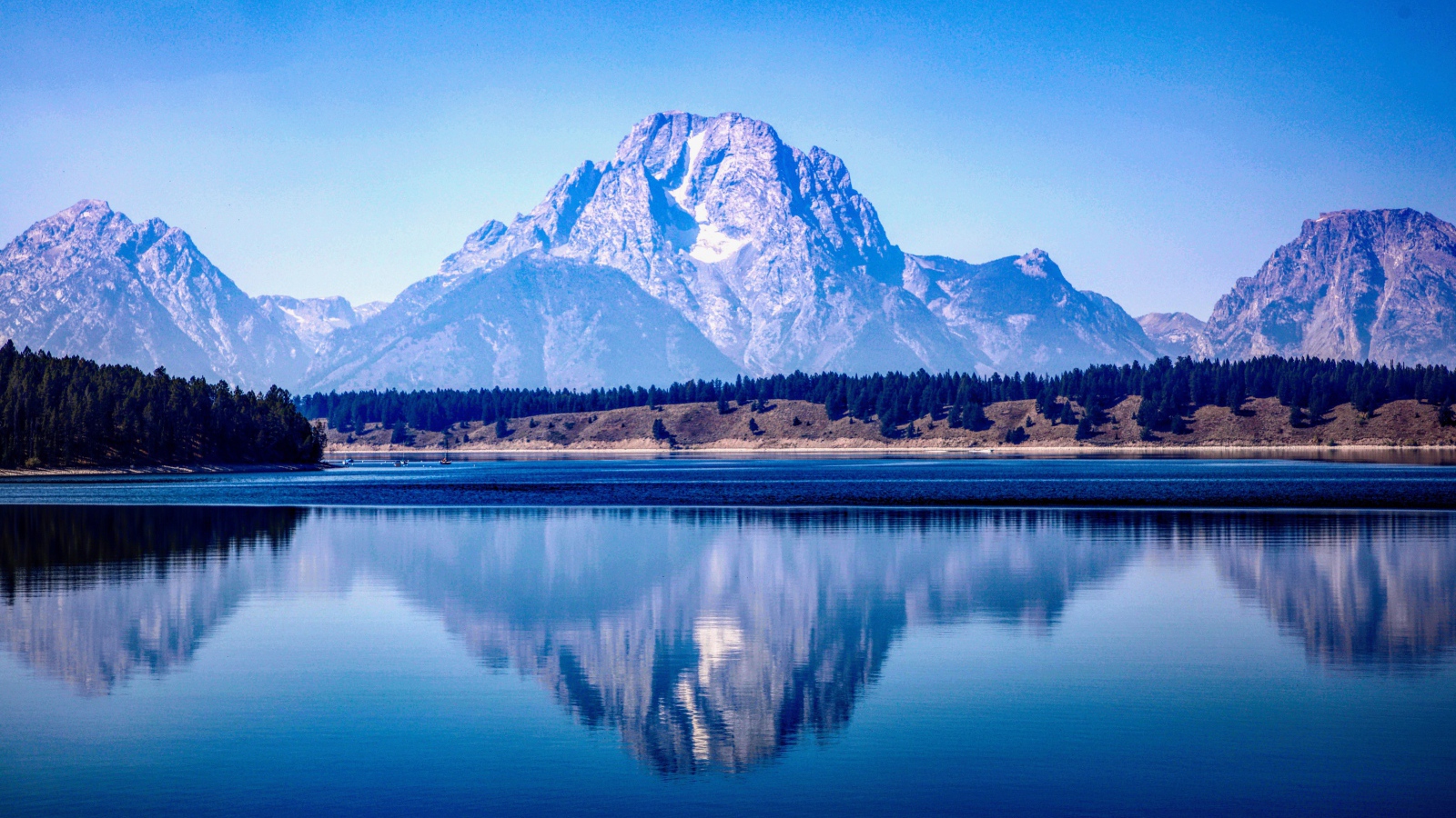 Высокие горы отражаются в озере под голубым небом