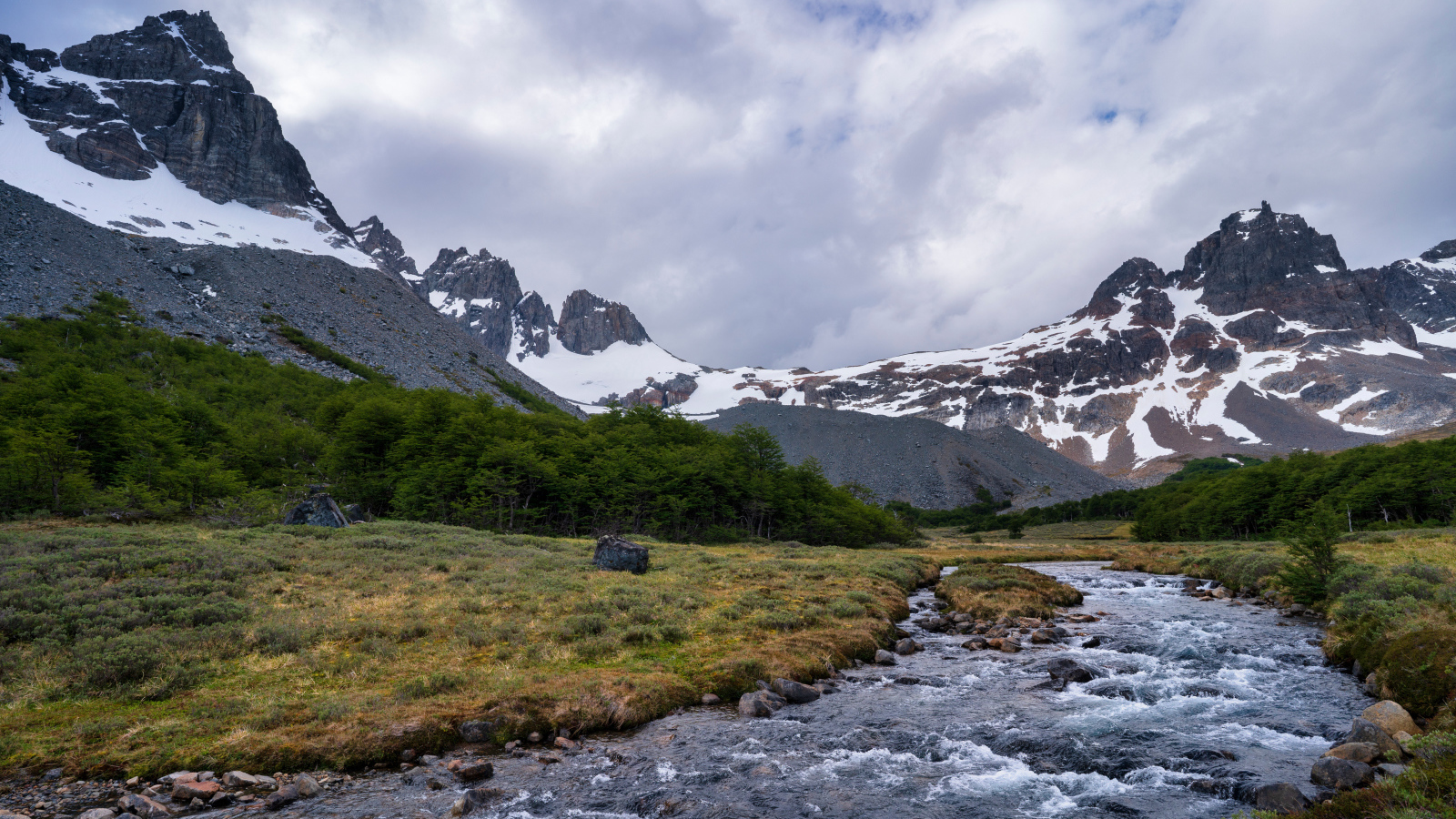 Быстрая река у заснеженных гор под густыми белыми облаками