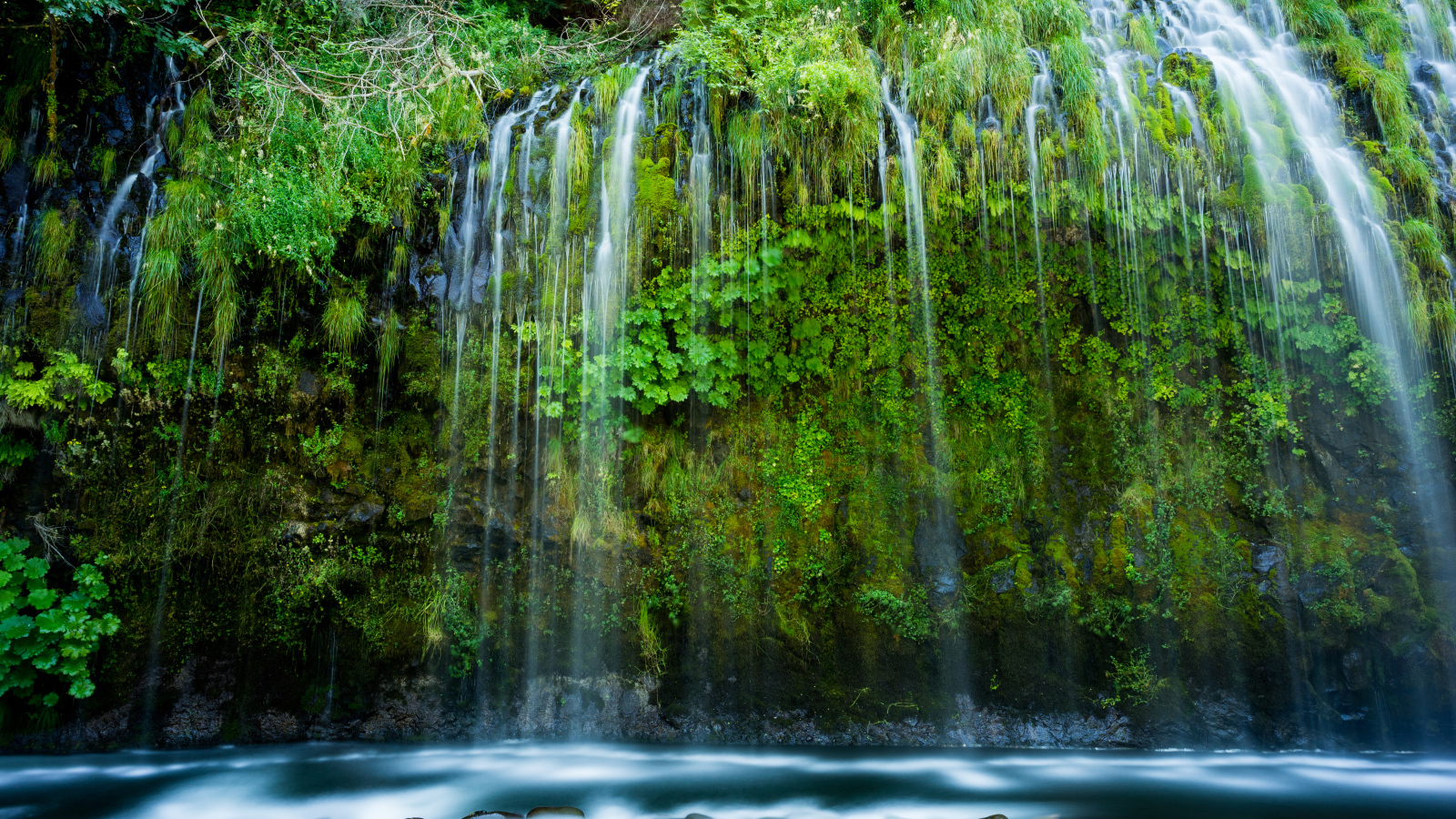 Красивый водопад стекает по покрытом зеленью утесе 