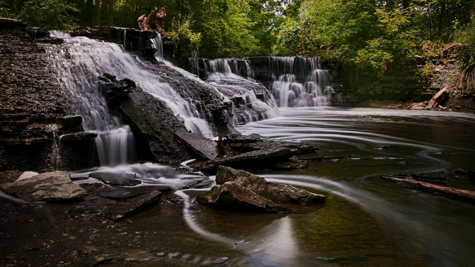 Быстрая вода стекает по камням водопада в парке 