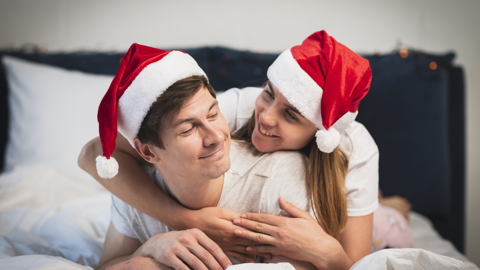 A man and a girl in Santa Claus hats lie on the bed