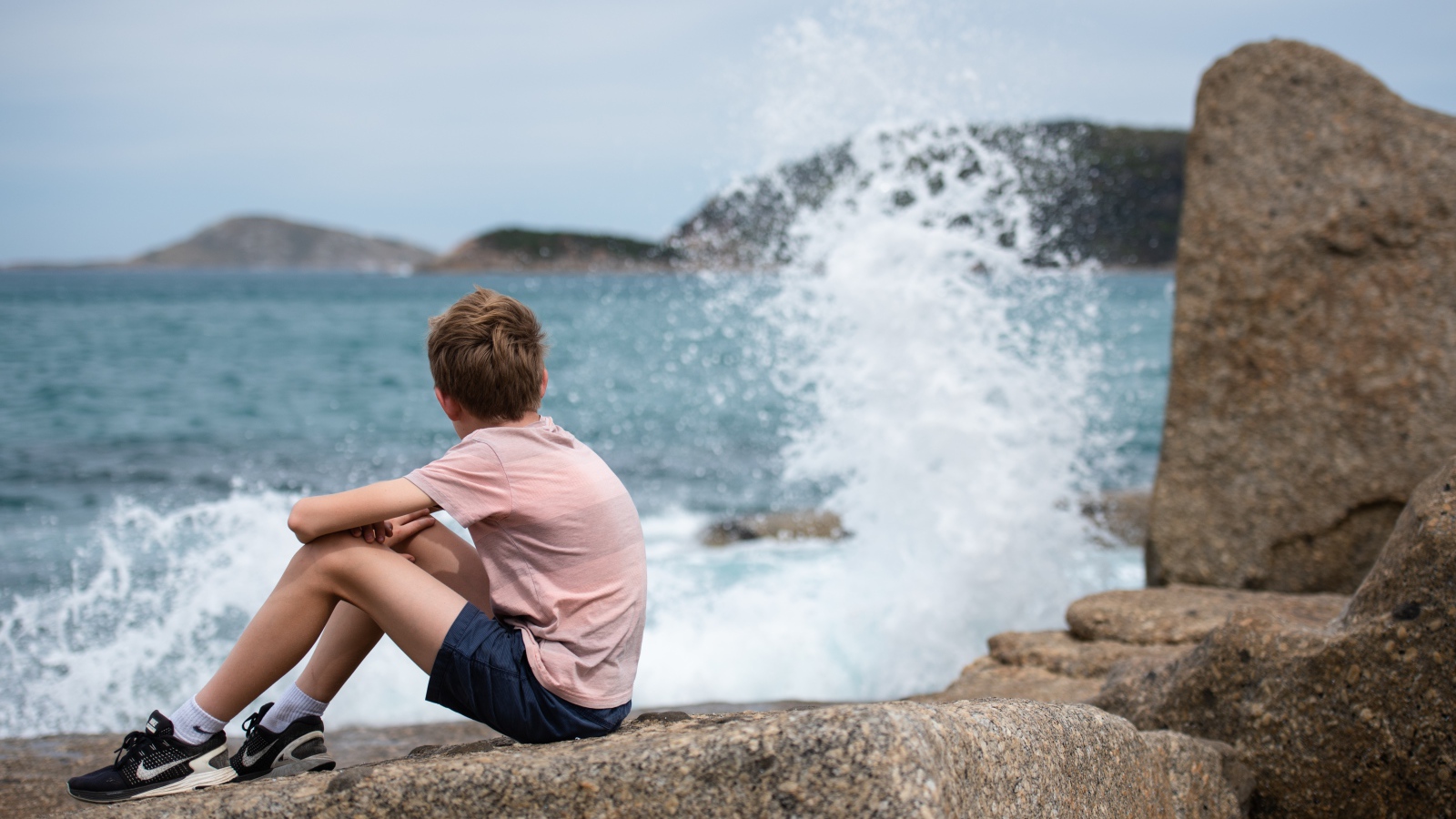 Мальчик сидит на камнях у бушующего моря