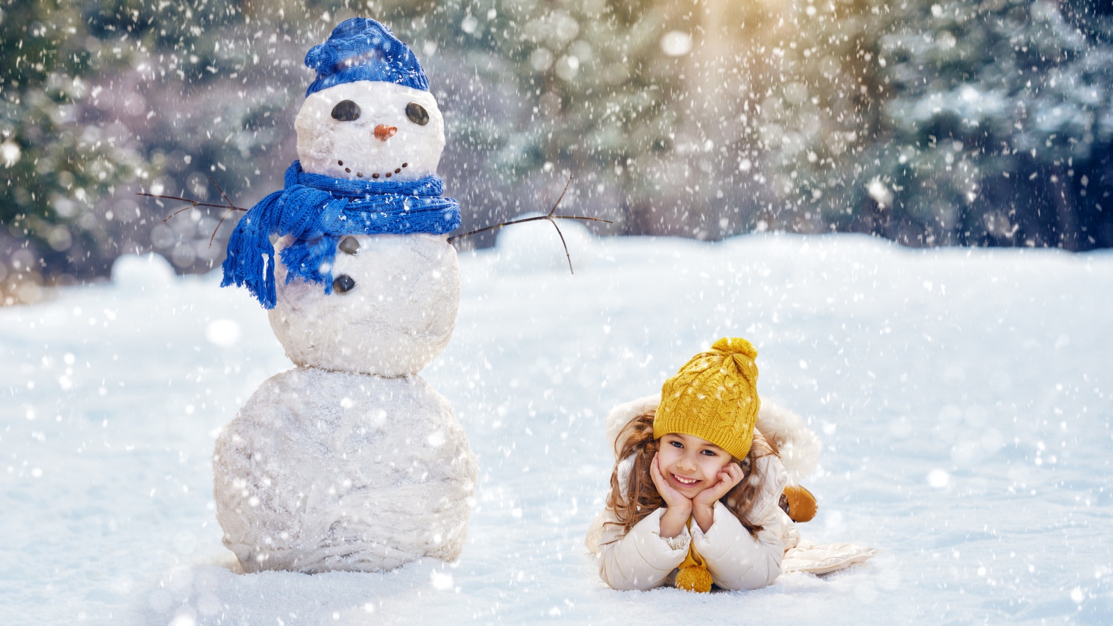 Милая девочка лежит на снегу у снеговика зимой