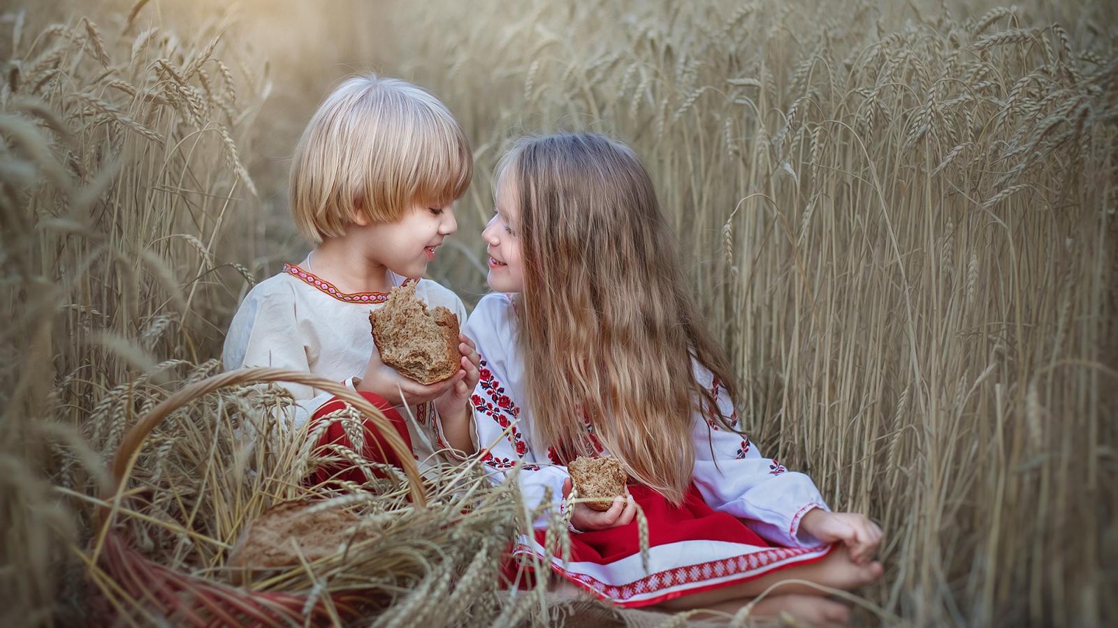 Маленькие мальчик и девочка с хлебом на пшеничном поле 