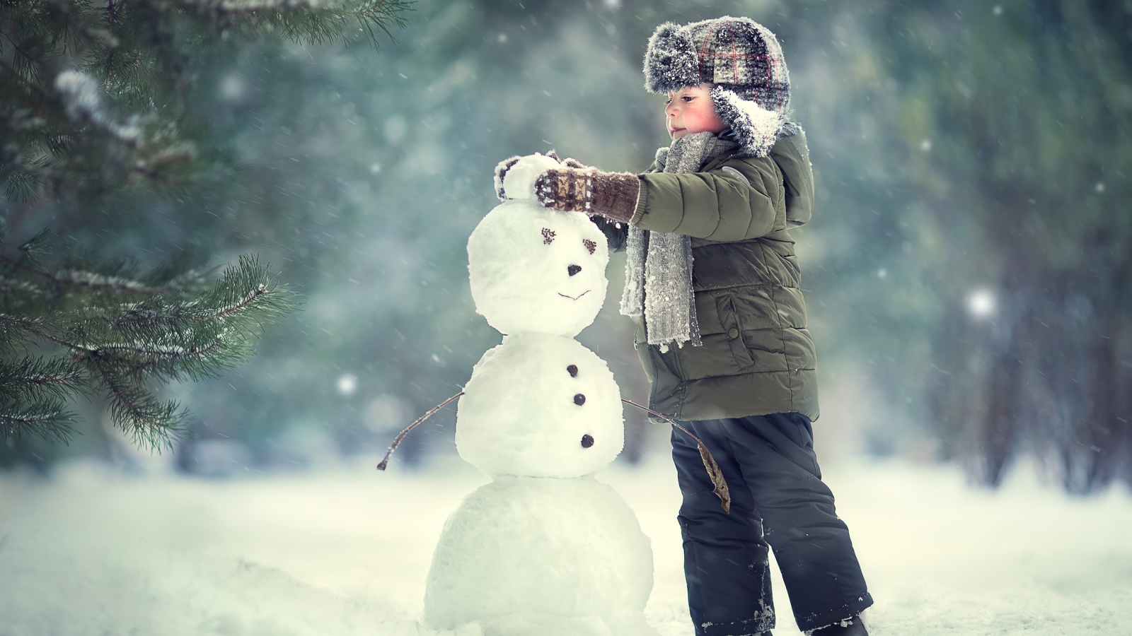 Маленький мальчик лепит снеговика зимой