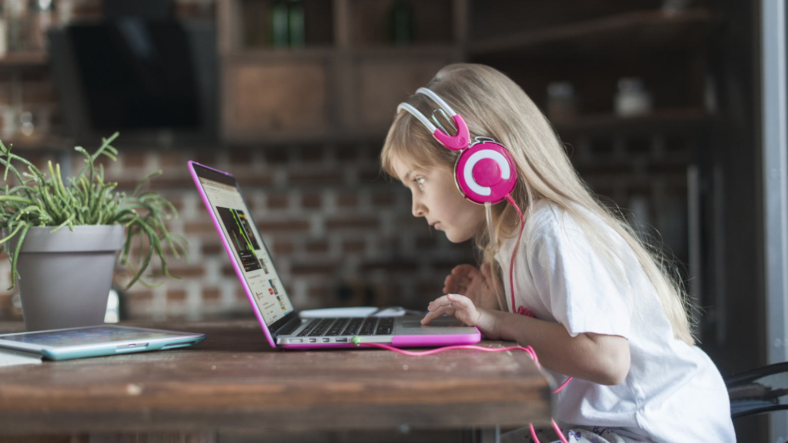 Маленькая девочка в наушниках сидит за ноутбуком