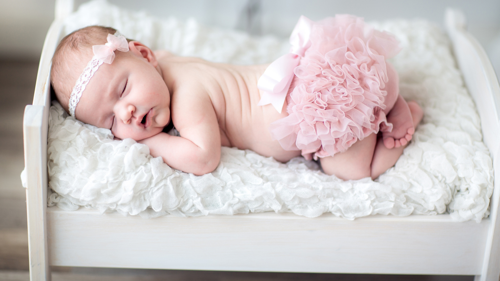 Маленькая спящая девочка в розовом костюме в кроватке