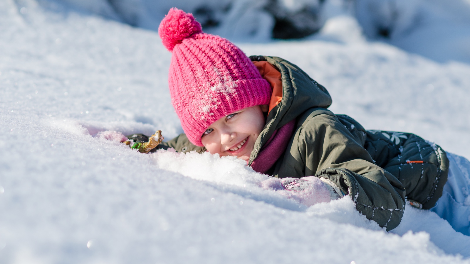 Маленькая улыбающаяся девочка лежит на снегу