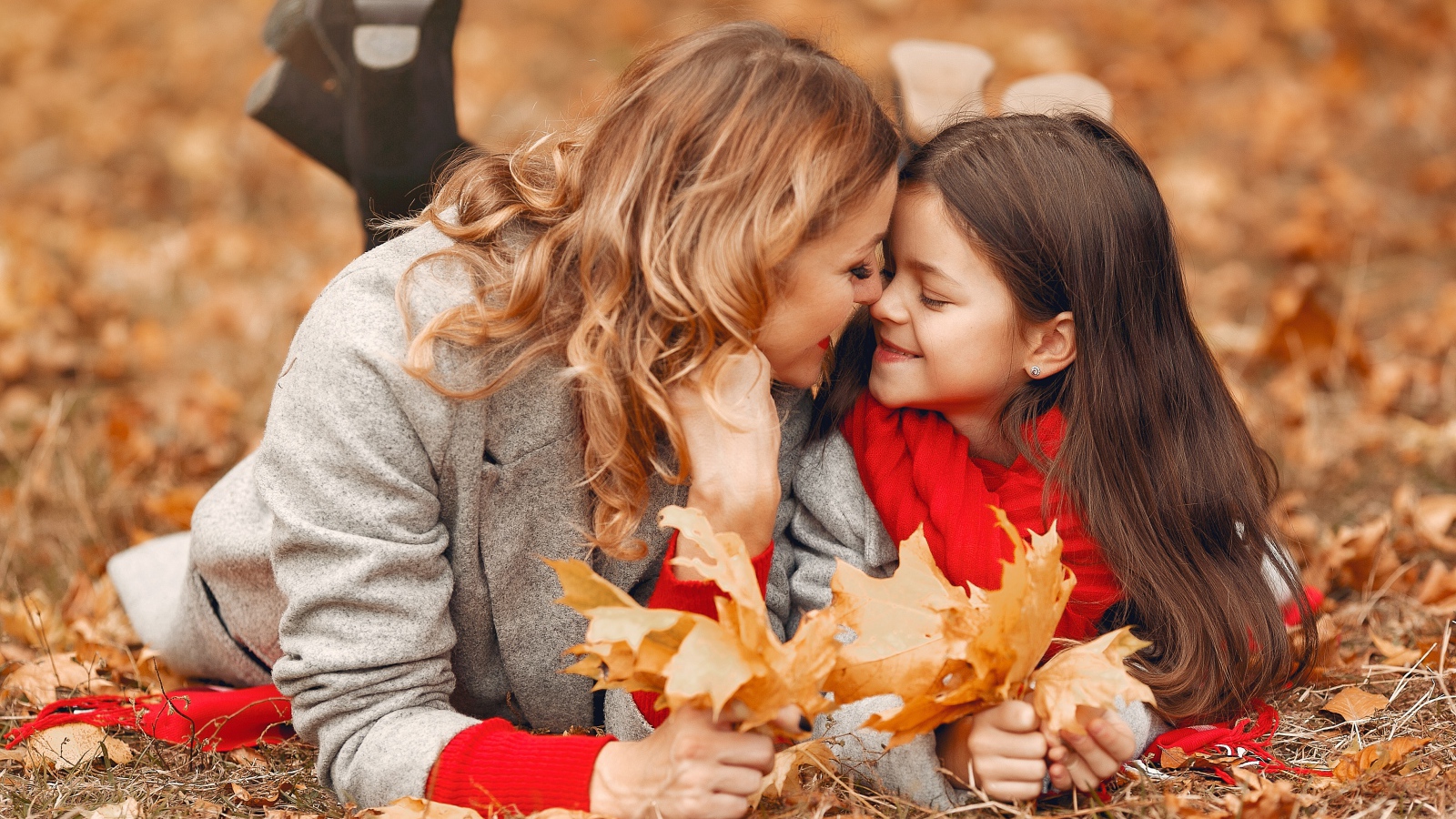 Мама с дочкой лежат на листве осенью 