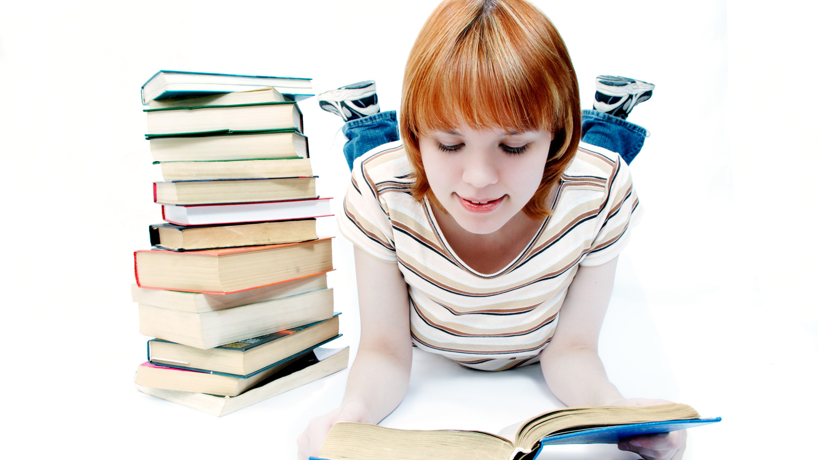 Рыжеволосая девочка школьница читает книги на белом фоне 