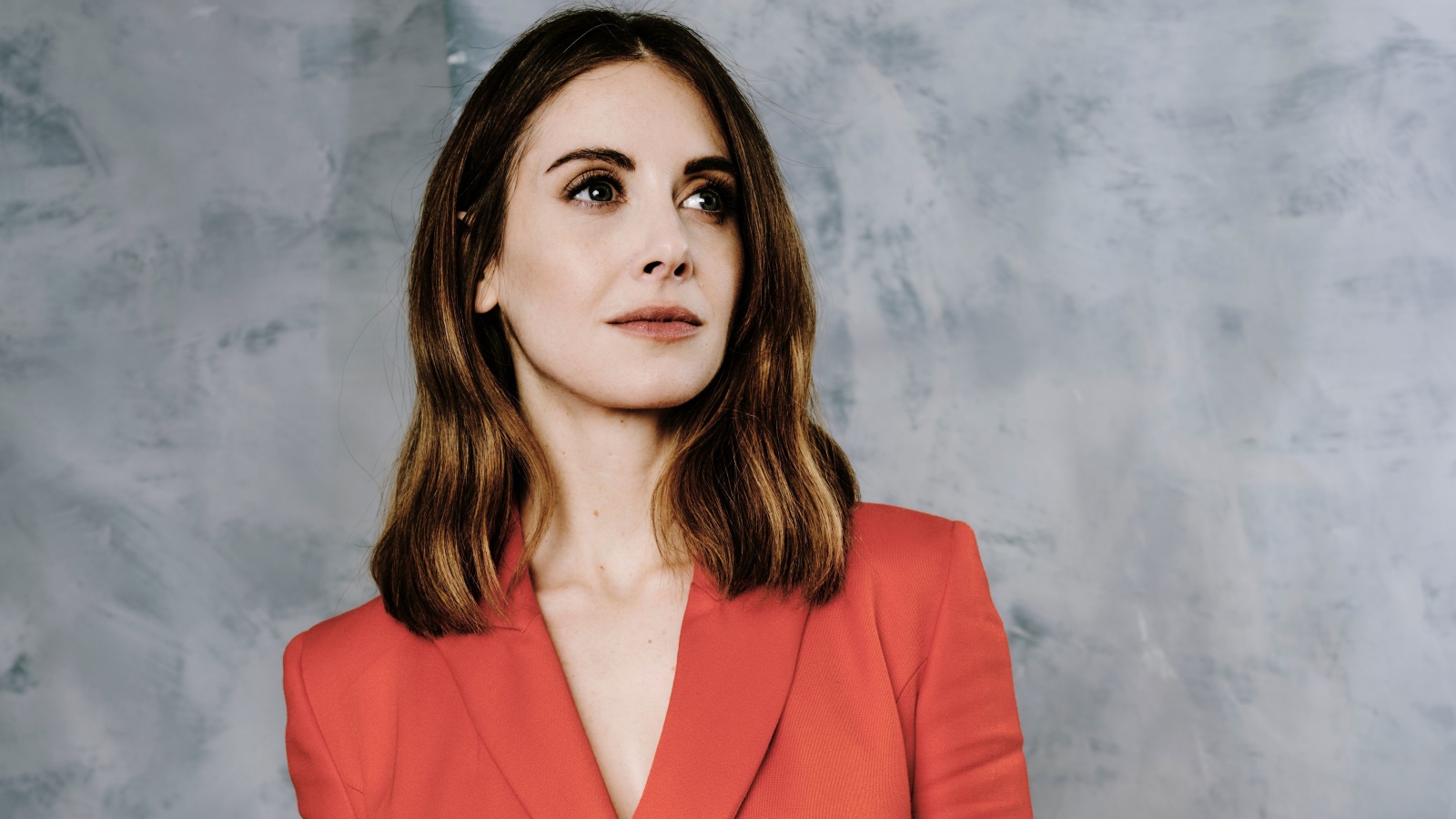 Актриса Элисон Бри в красном пиджаке на сером фоне