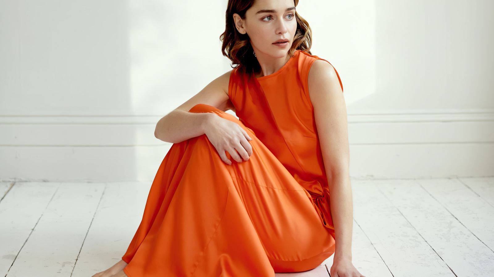 Актриса Эмилия Кларк  в оранжевом платье сидит на полу