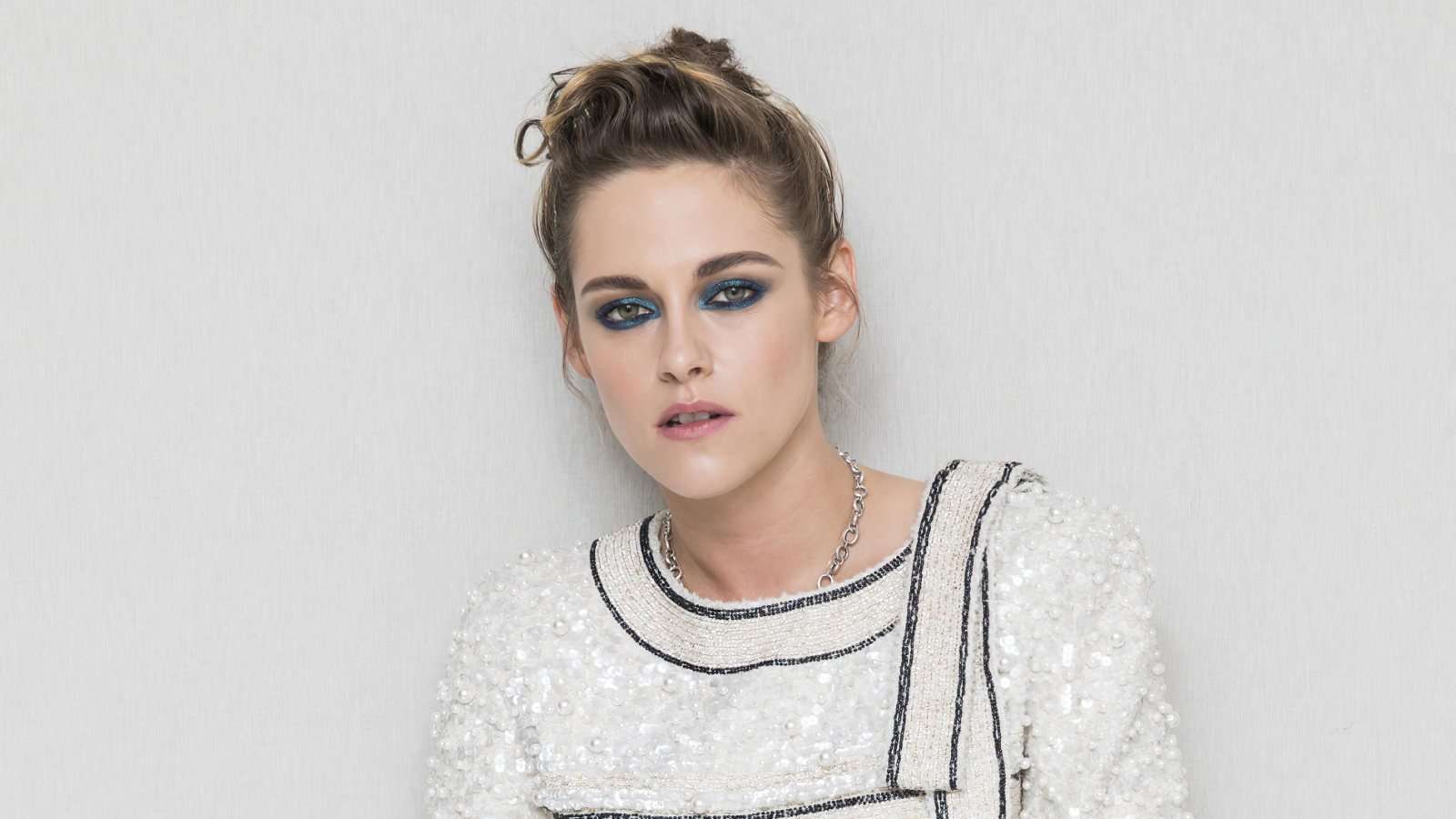 Актриса Кристен Стюарт с накрашенными глазами на фоне серой стены 