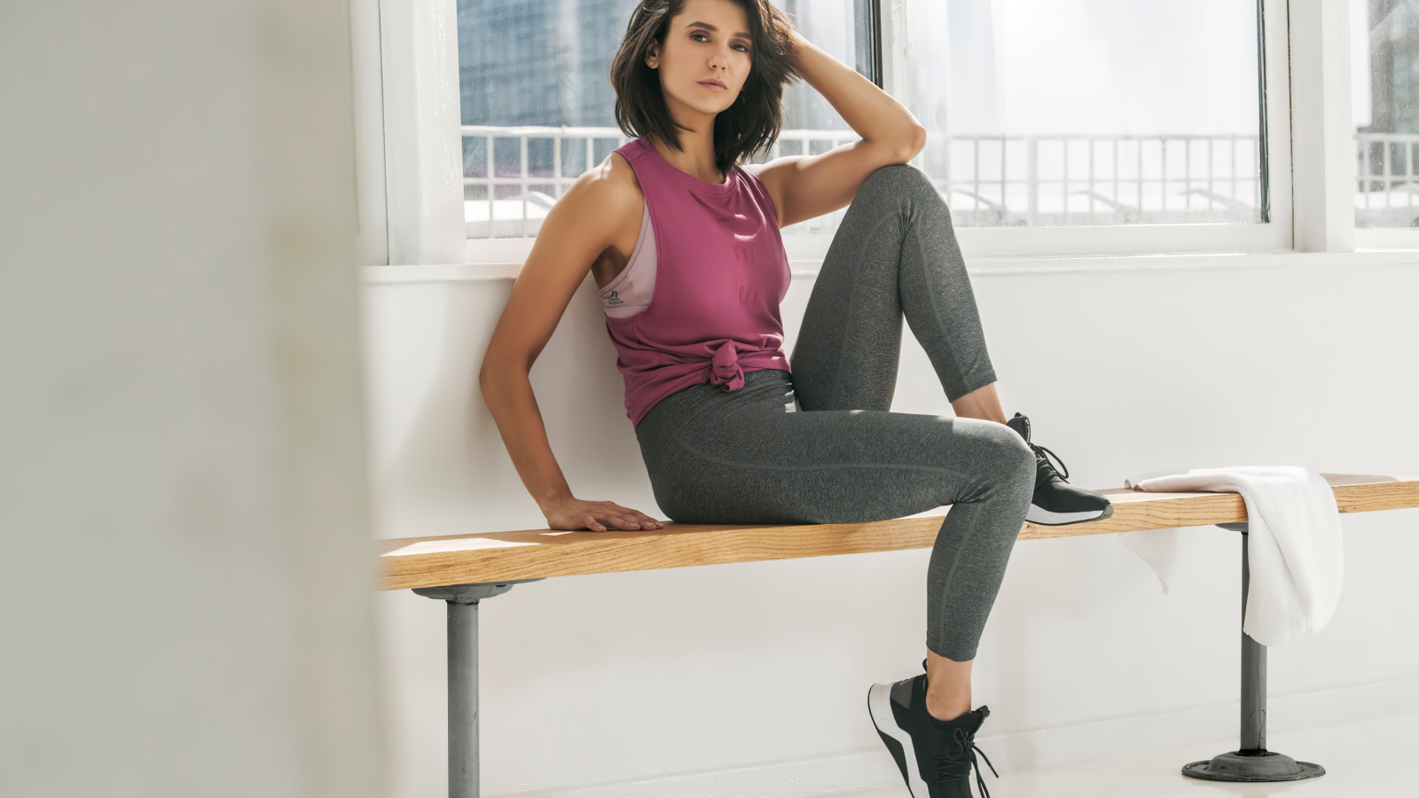 Актриса Нина Добрев сидит на лавке в спортивном костюме
