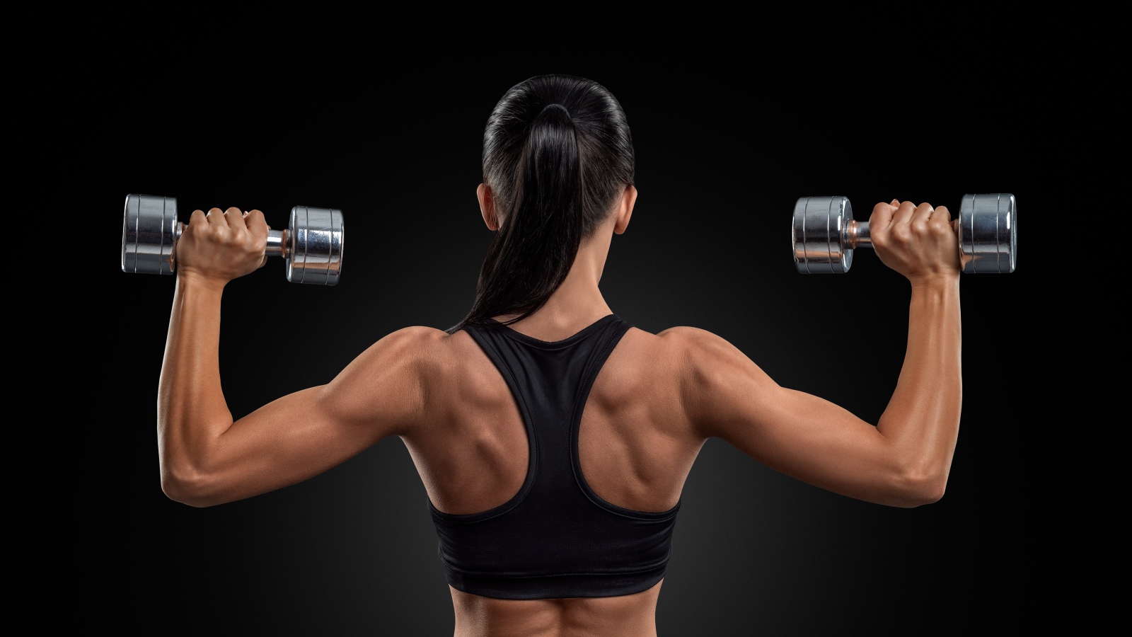 Стройная спортивная девушка с гантелями в руках на черном фоне