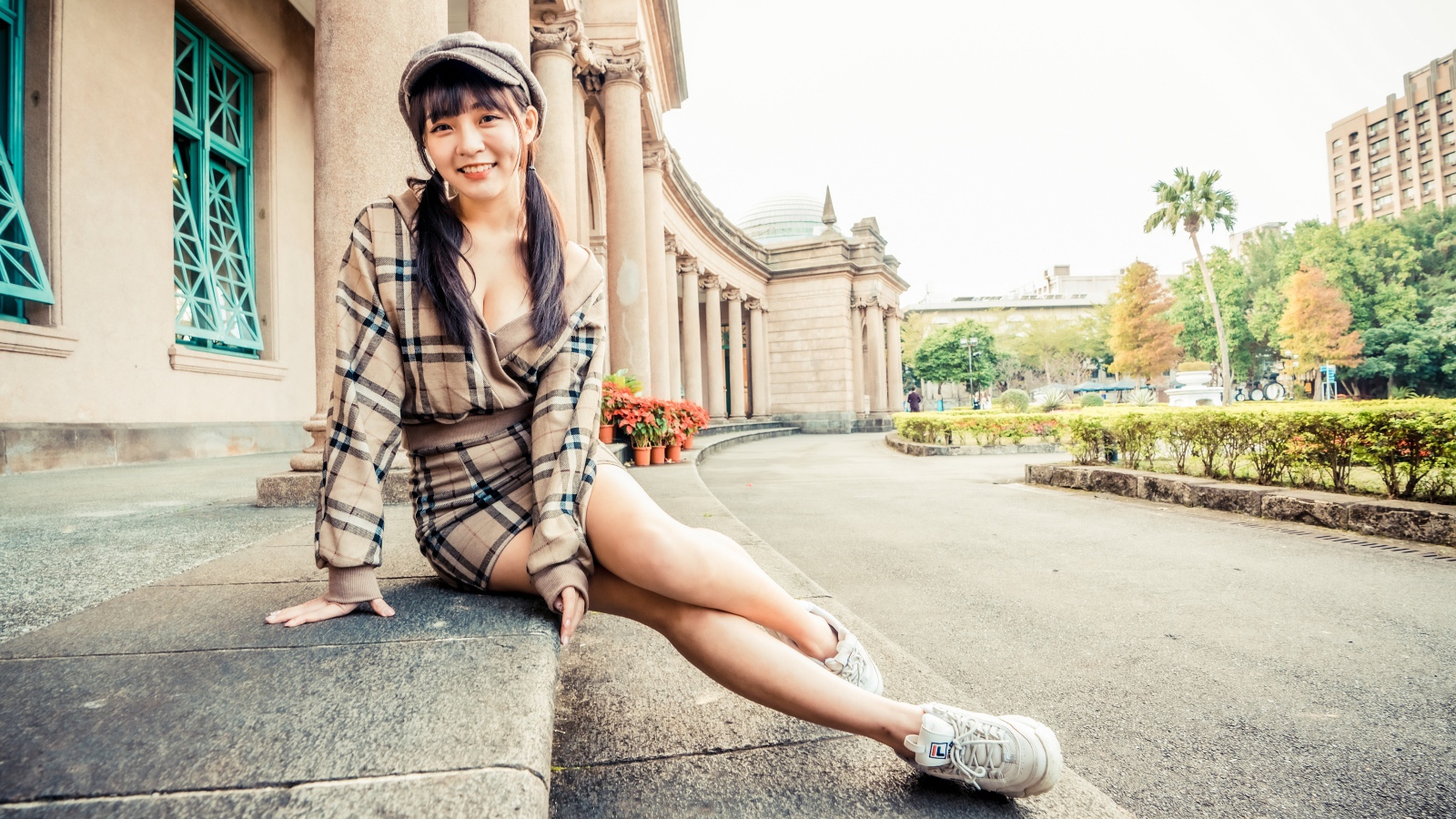 Улыбающаяся азиатка в кепке сидит на ступеньках 