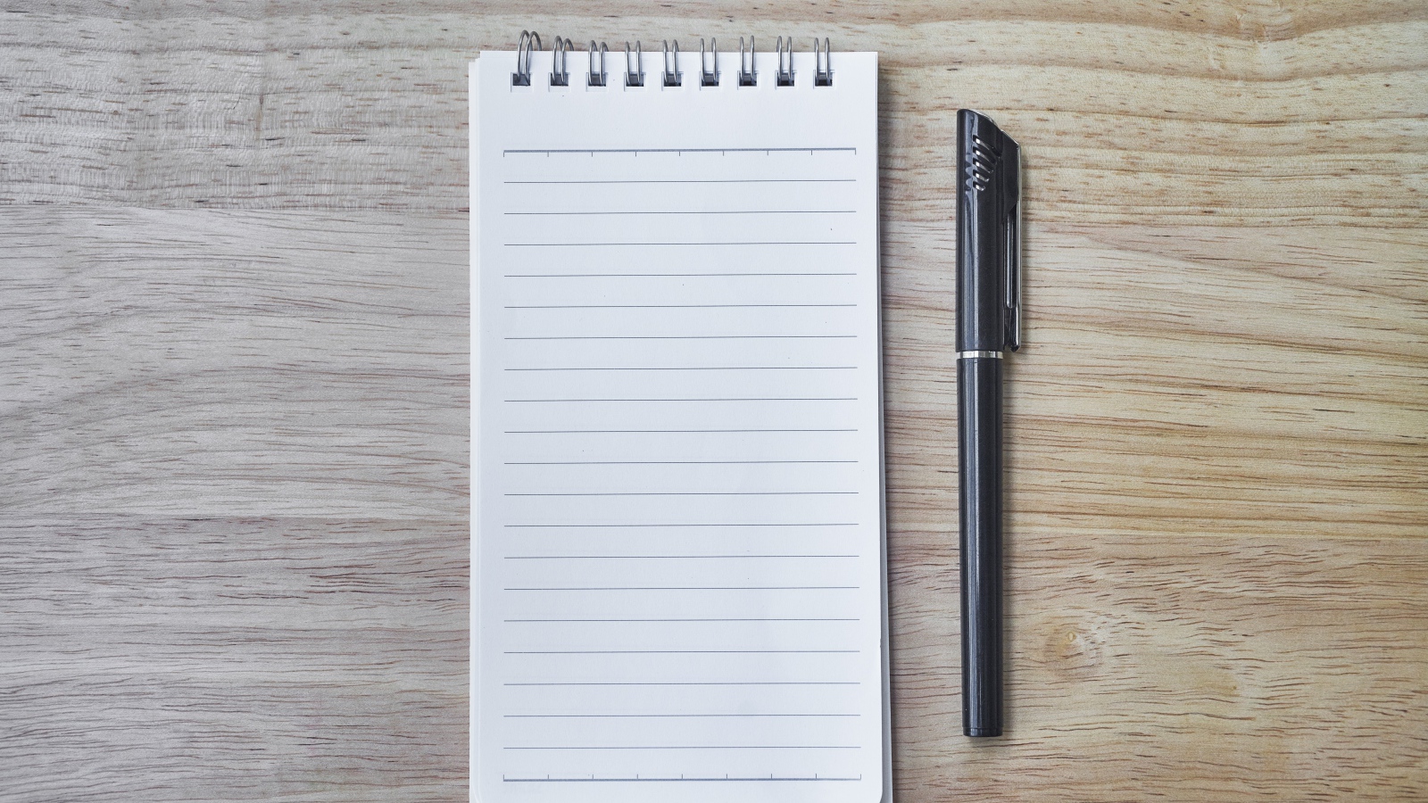 Авторучка и блокнот лежат на деревянном столе