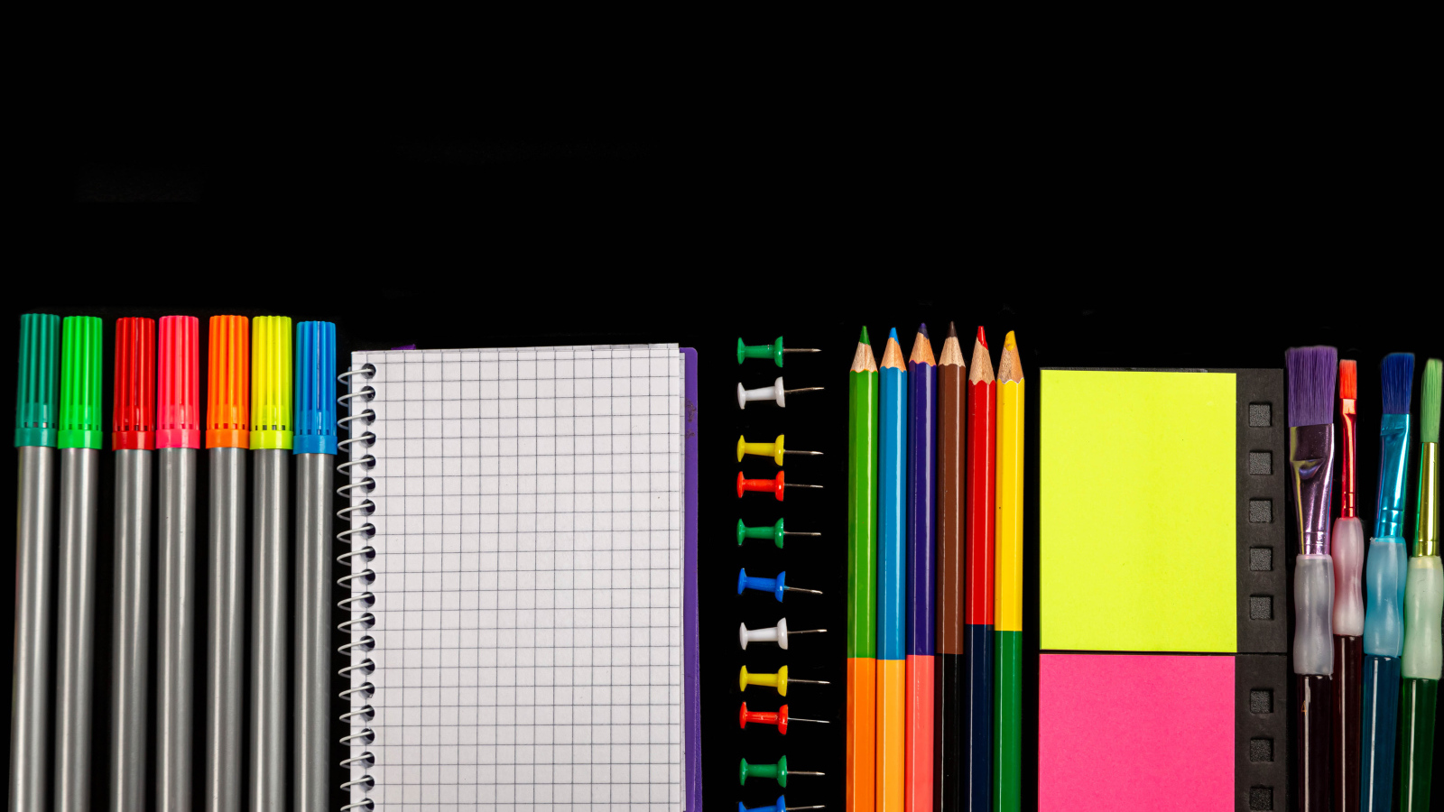 Felt pens, pencils, notebook and brushes on black background