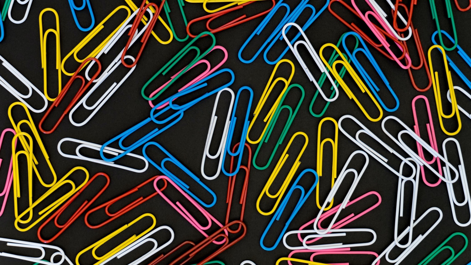 Many multi-colored paper clips on a black background