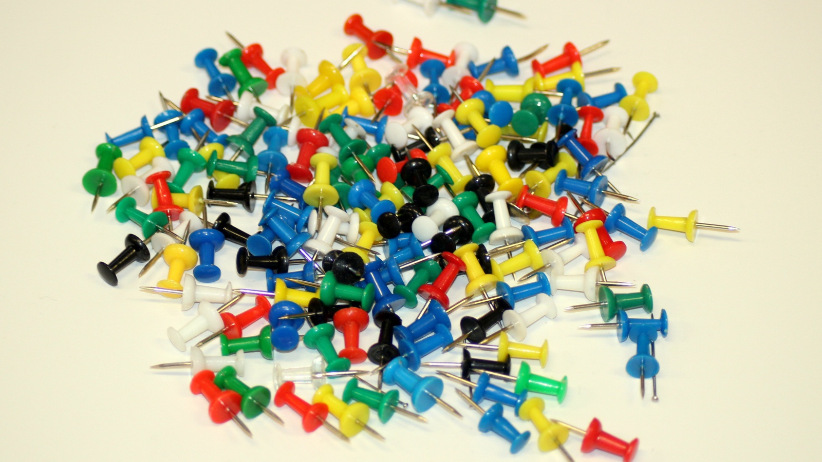 Разноцветные канцелярские гвозди на белом фоне