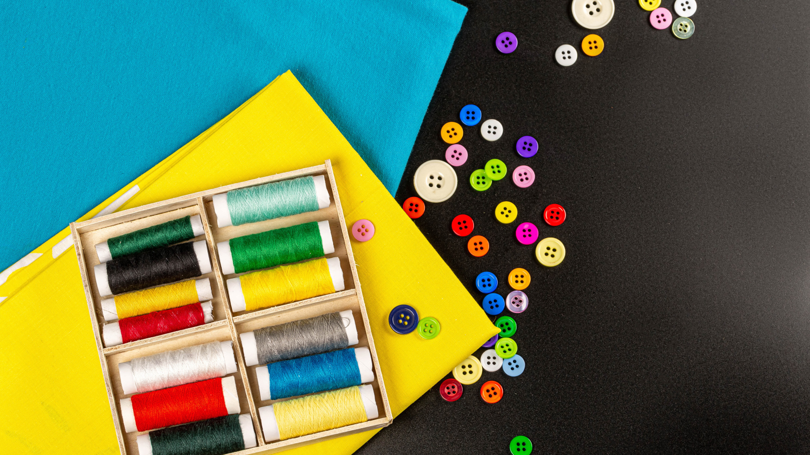 Разноцветные нитки, пуговицы и бумага на черном фоне 