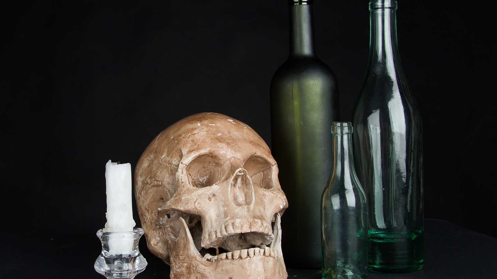 Череп, пустые бутылки и свеча на черном фоне