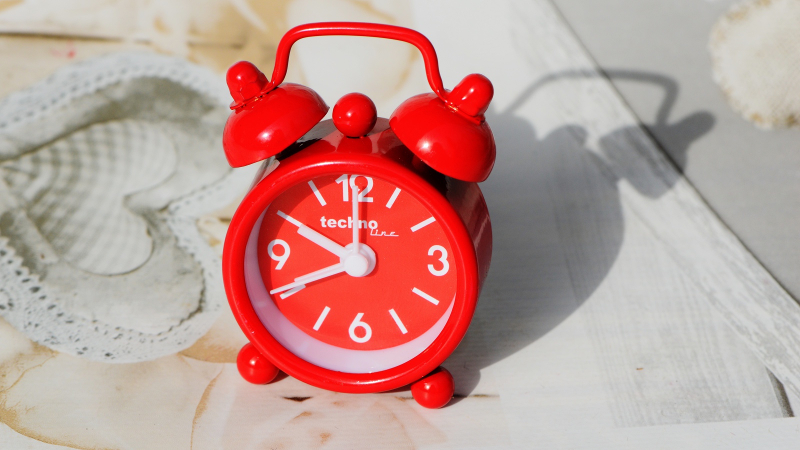 Маленький красный будильник стоит на столе 