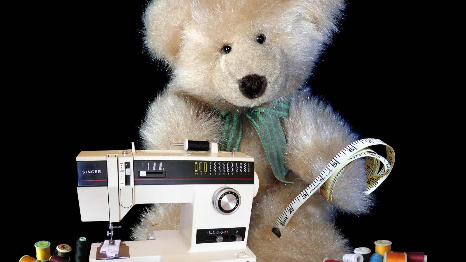 Игрушечный медвежонок со швейной машинкой на черном фоне 