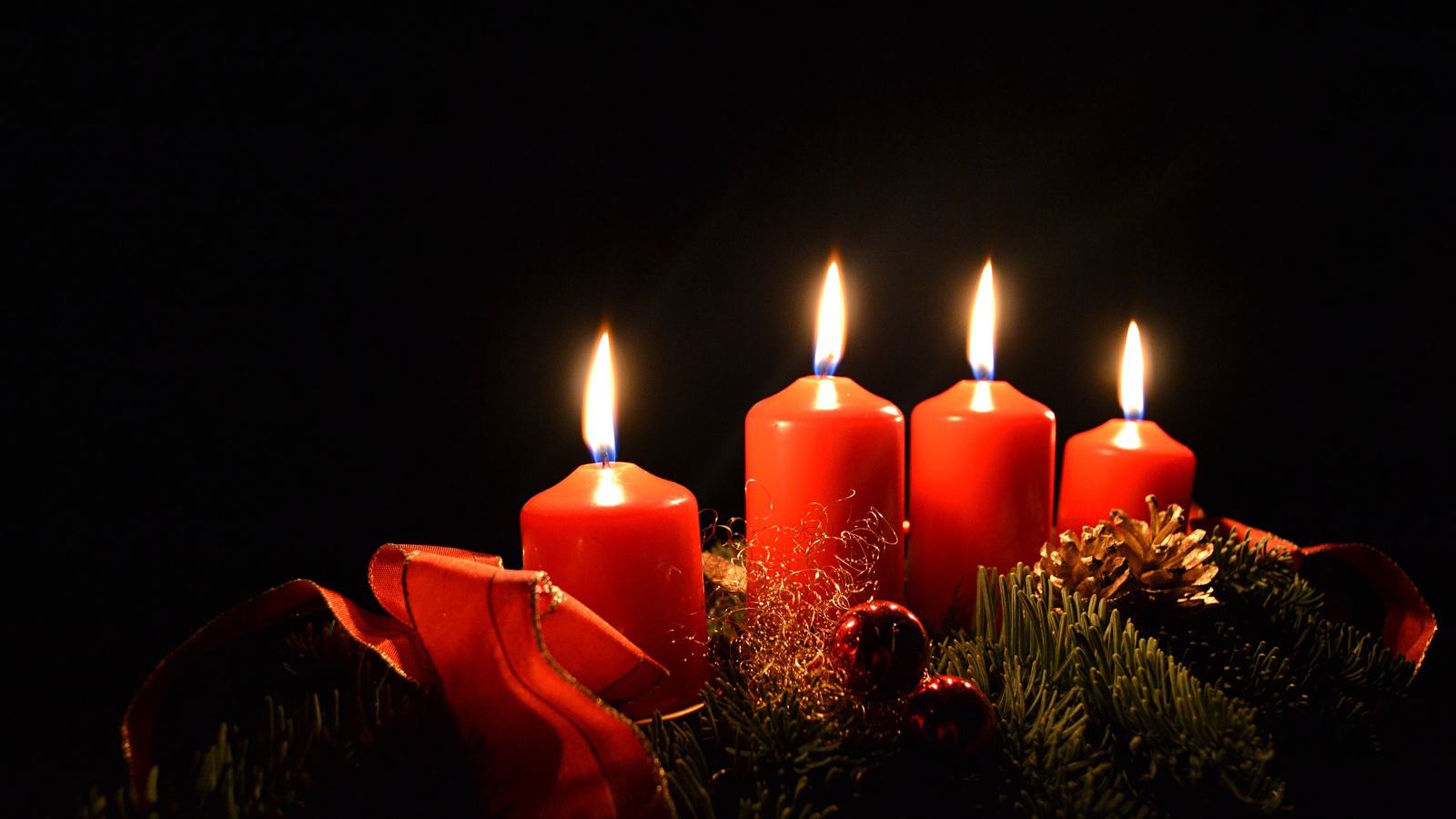Три зажженные красные свечи с еловой веткой на черном фоне 