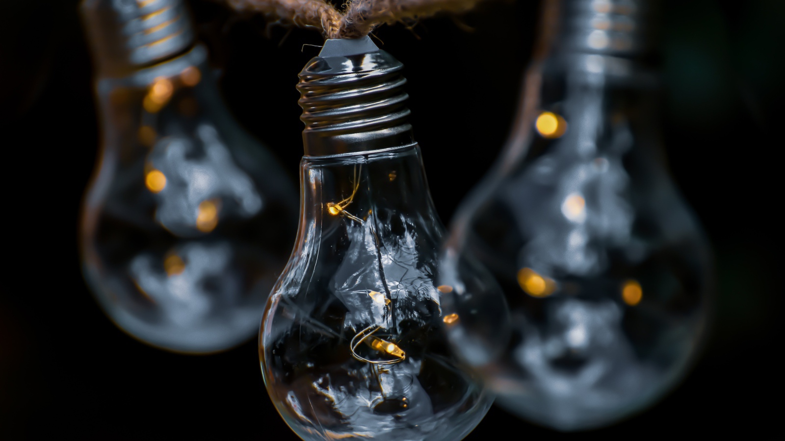 Три лампочки висят на веревке на черном фоне