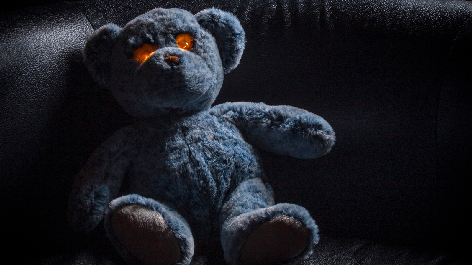 Игрушка со светящимися глазами на черном диване