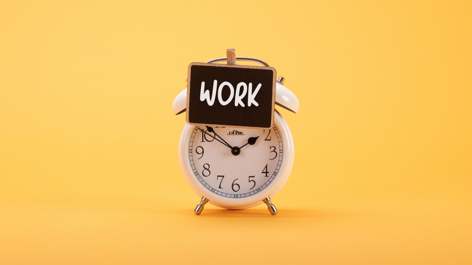 Белый будильник с табличкой на желтом фоне