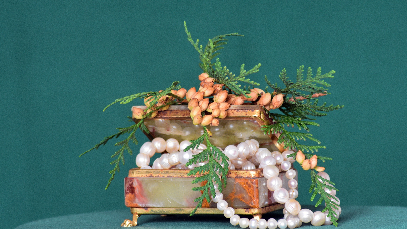 Шкатулка с бусами из жемчуга на зеленом фоне 