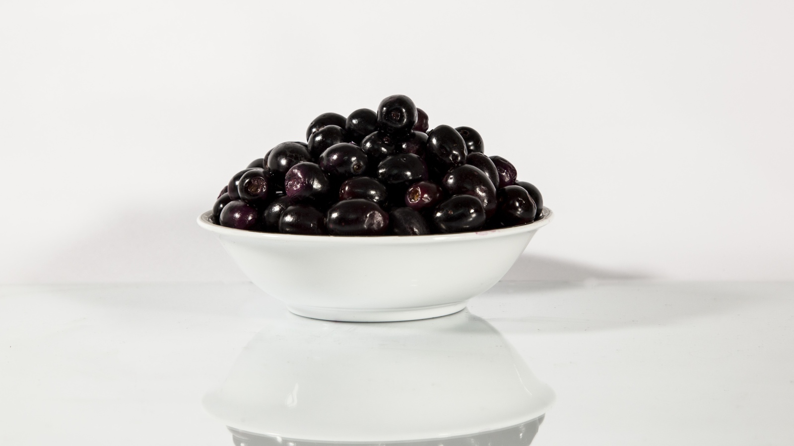 Черные оливки в белой тарелке отражаются в поверхности