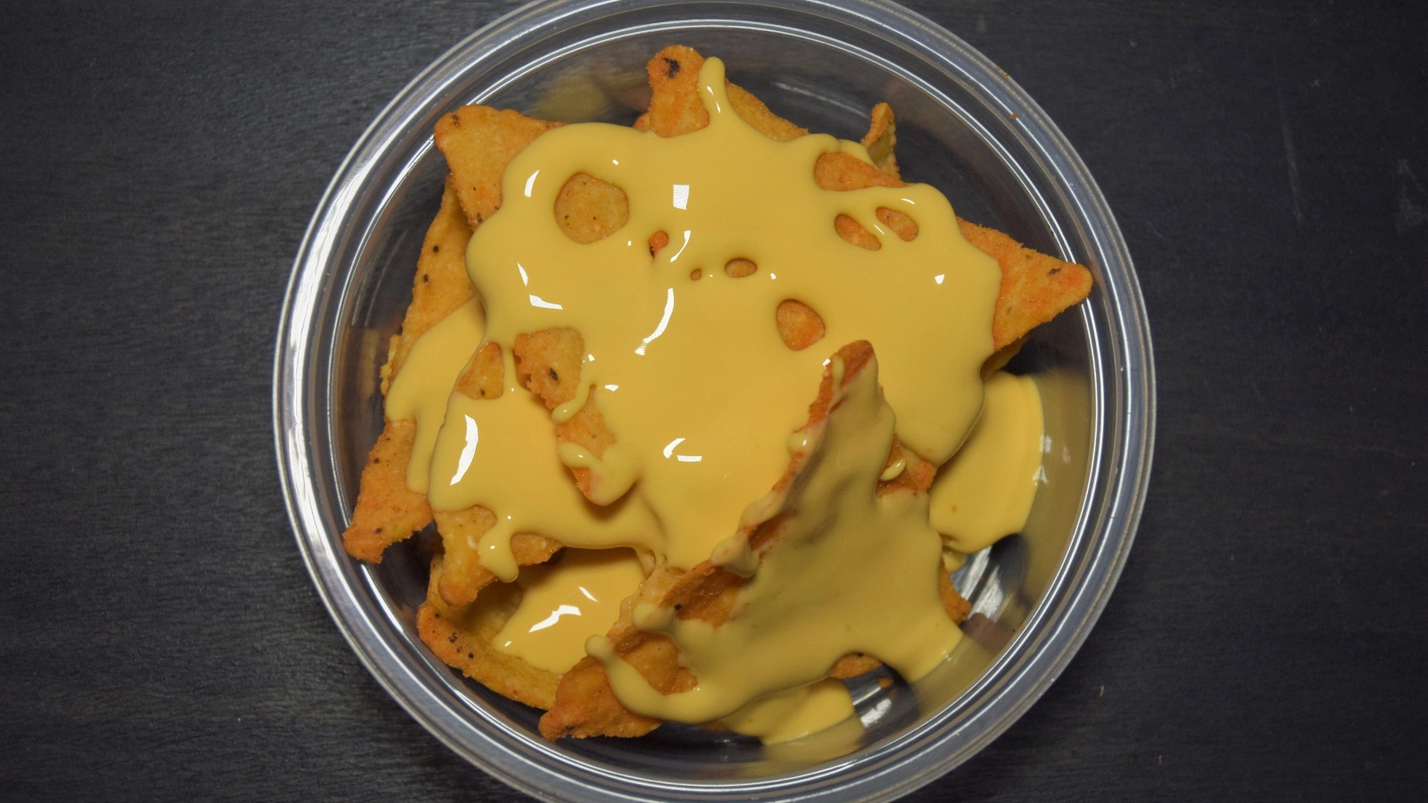 Чипсы начос с сырным соусом в миске на черном фоне