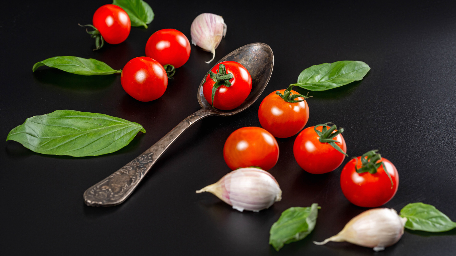 Красные помидоры с чесноком и листьями базилика на столе 