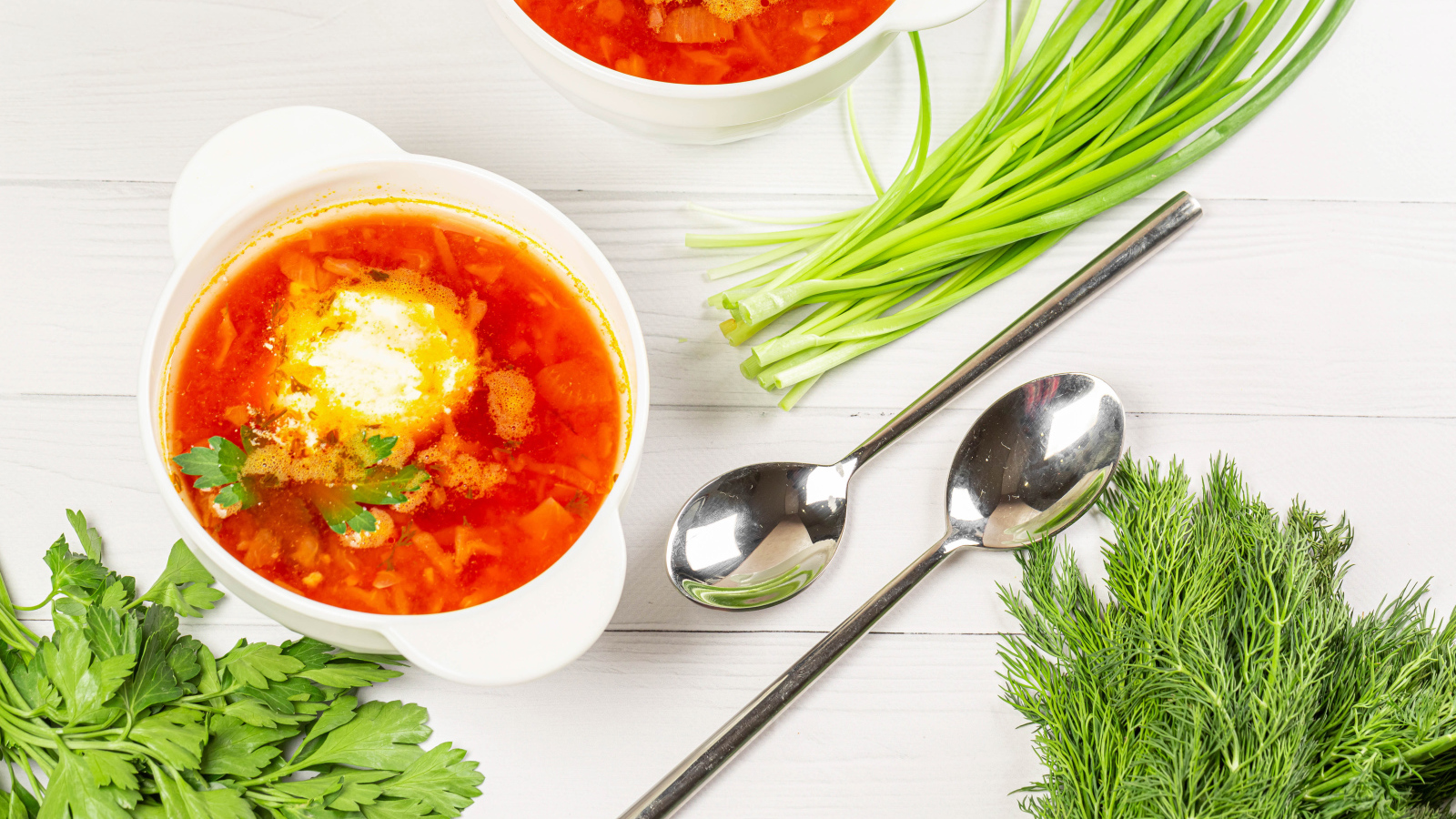 Две тарелки борща на столе с зеленью петрушки, луком и укропом