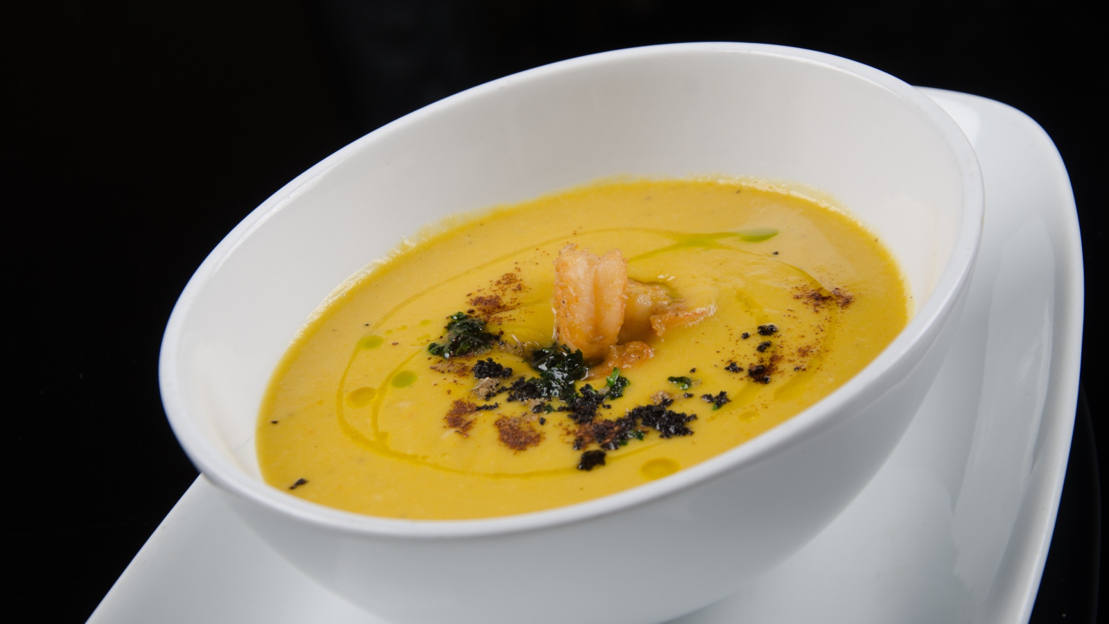 Желтый суп пюре в белой тарелке на черном фоне