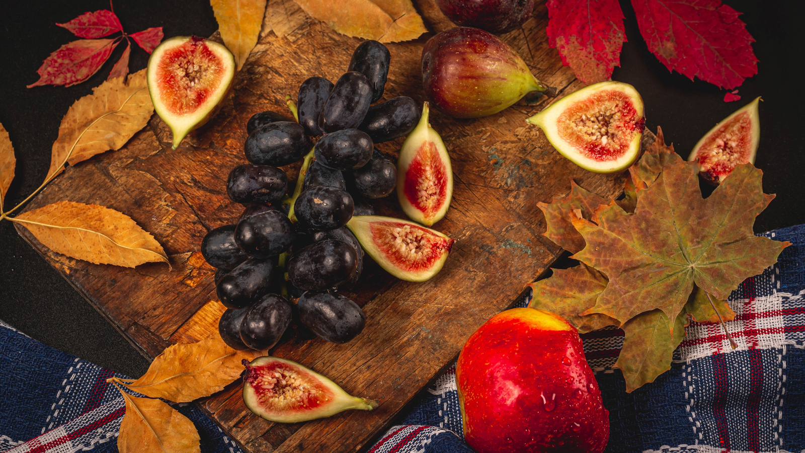 Синий виноград и плоды инжира на столе с листьями
