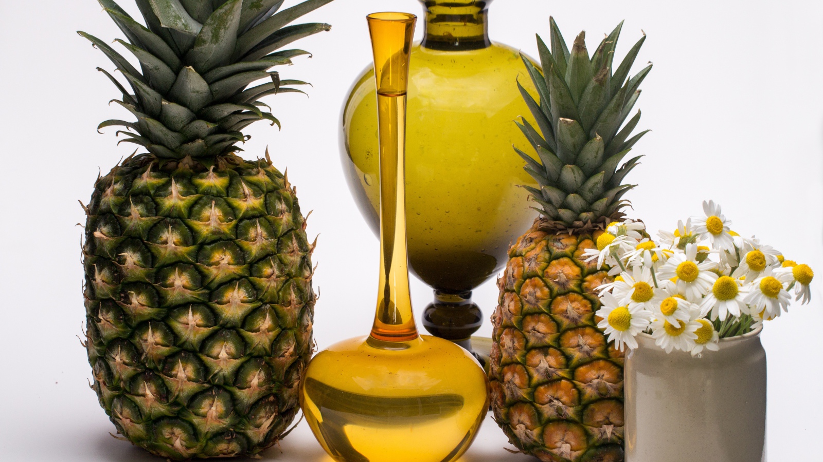 Ананасы на столе с маслом и ромашками