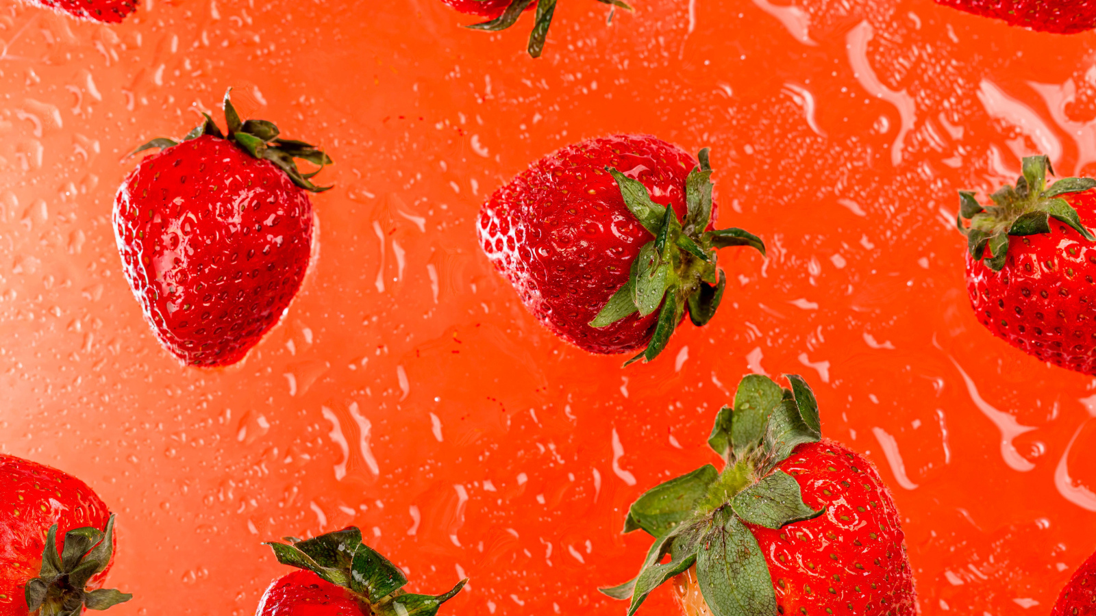 Красная клубника в воде на оранжевом фоне 