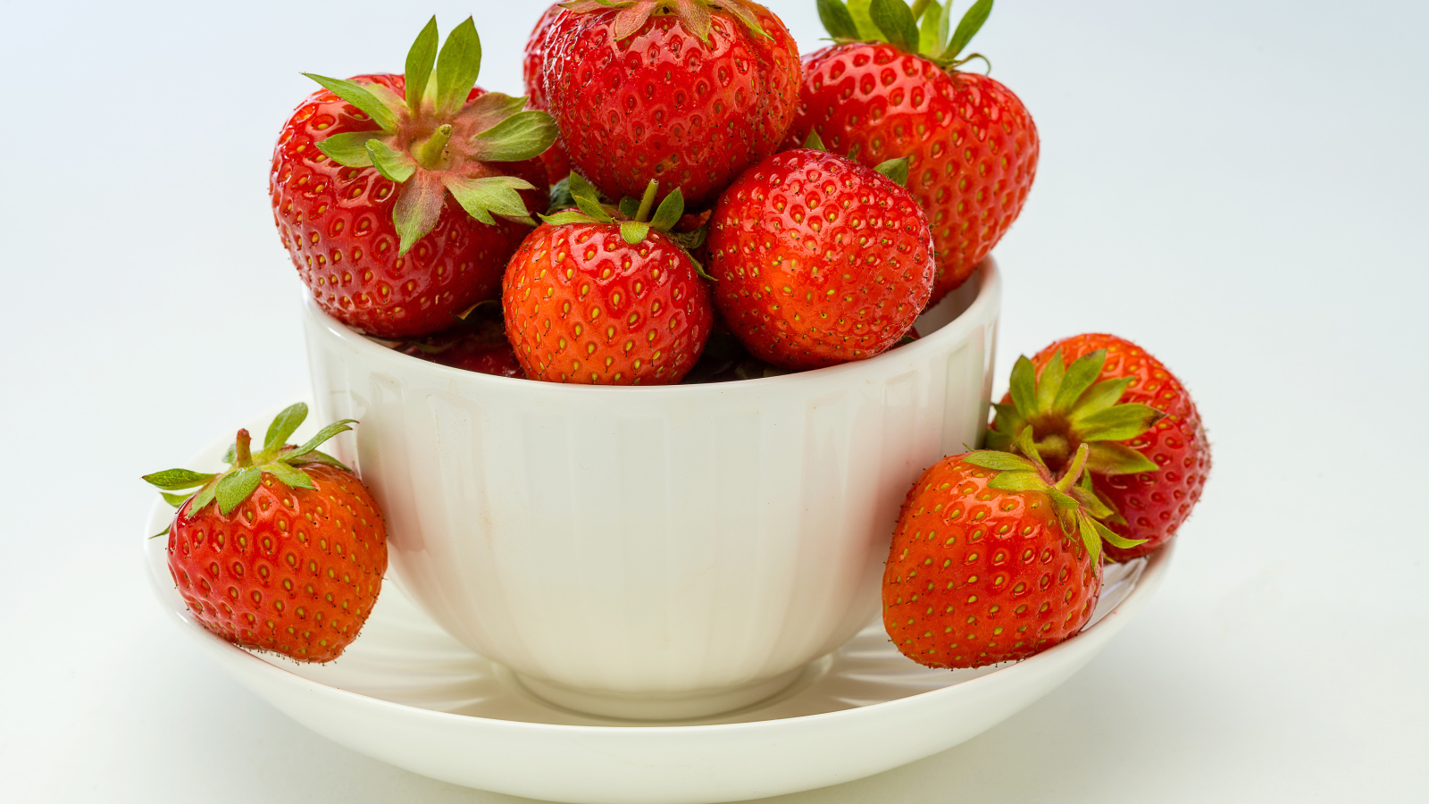 Спелая красная клубника в белой миске с блюдцем