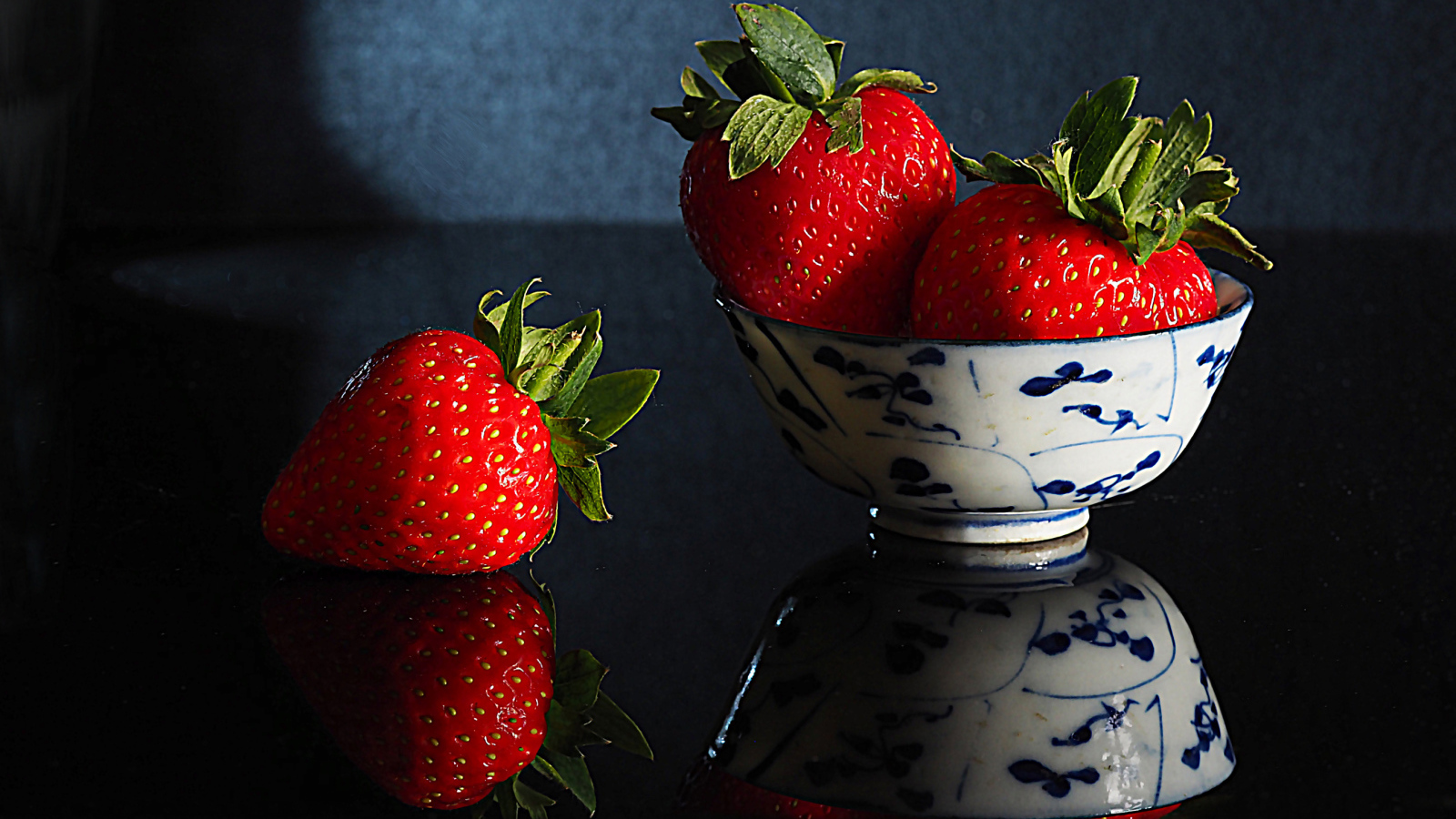 Три красные клубники в миске на столе