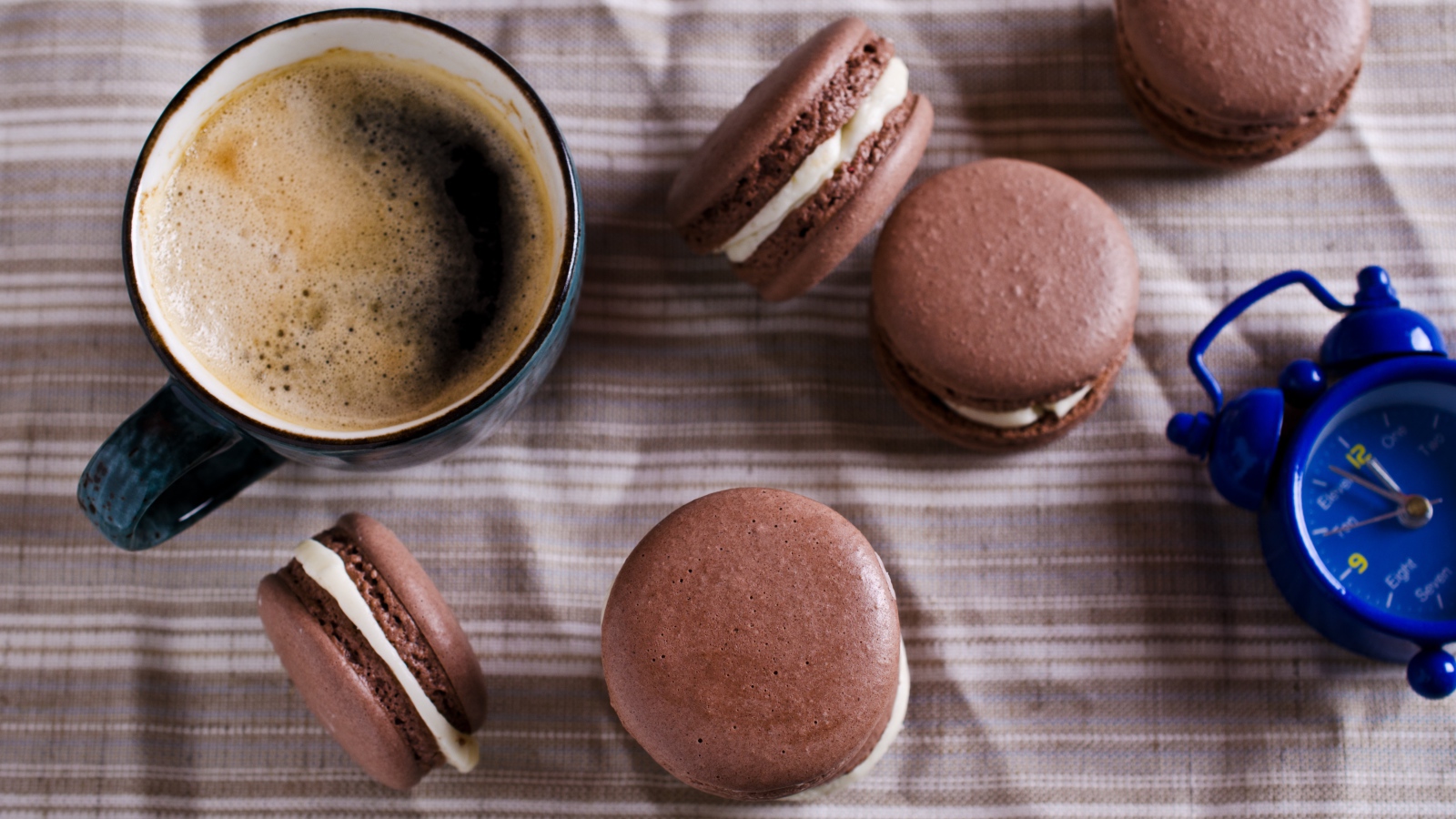 Чашка кофе на столе с десертом макарун и будильником